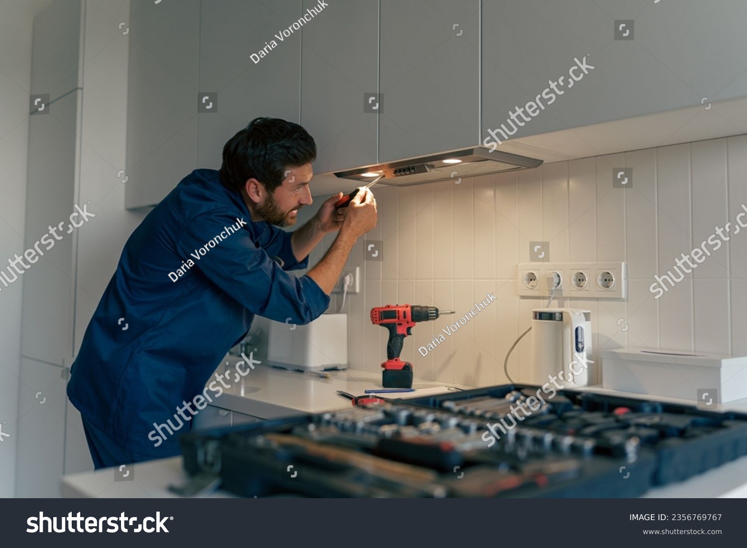 Professional male worker in uniform repairing modern cooker hood in kitchen #2356769767