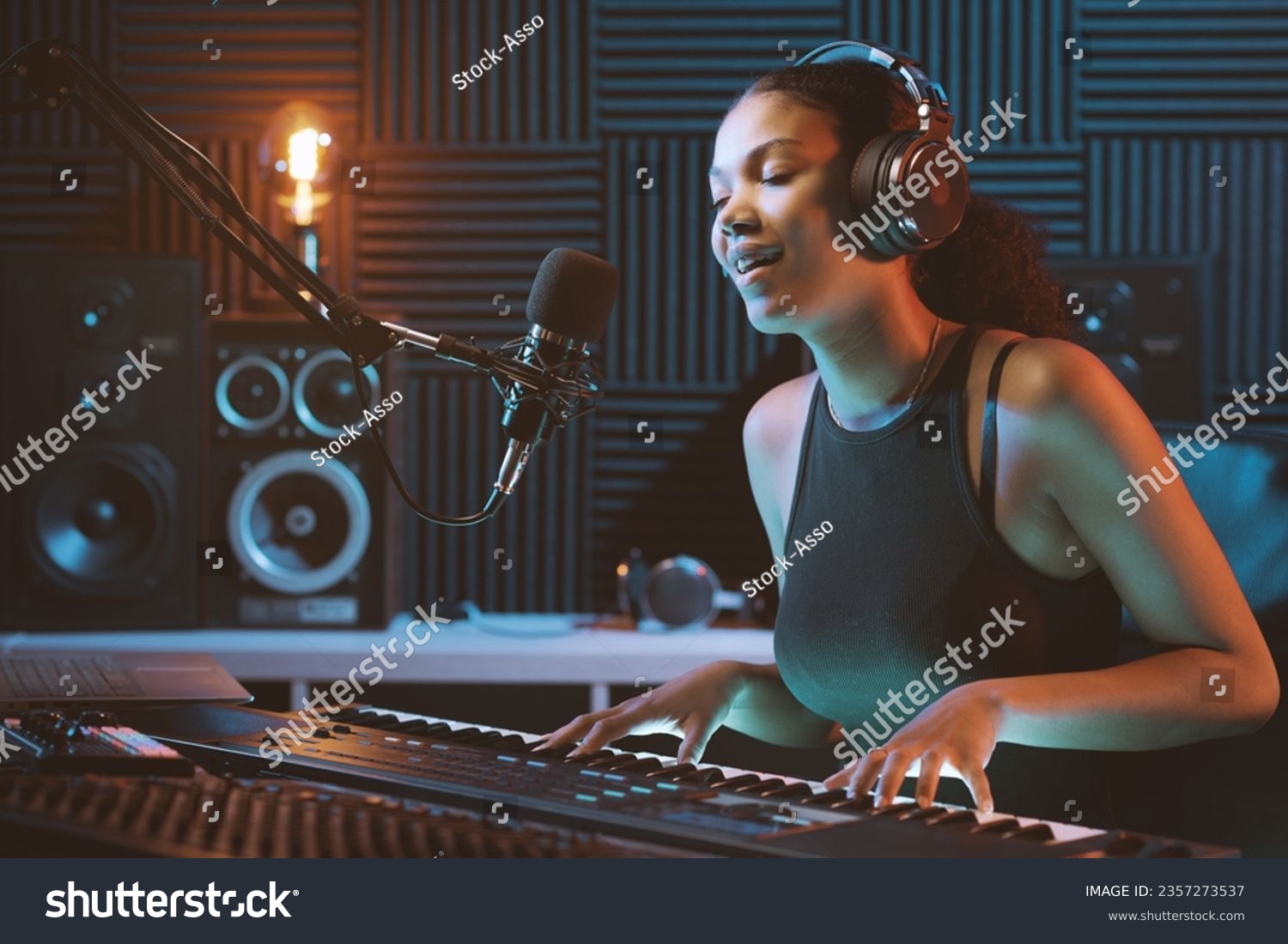 Young female artist recording a song in the studio, she is singing and playing the keyboard #2357273537