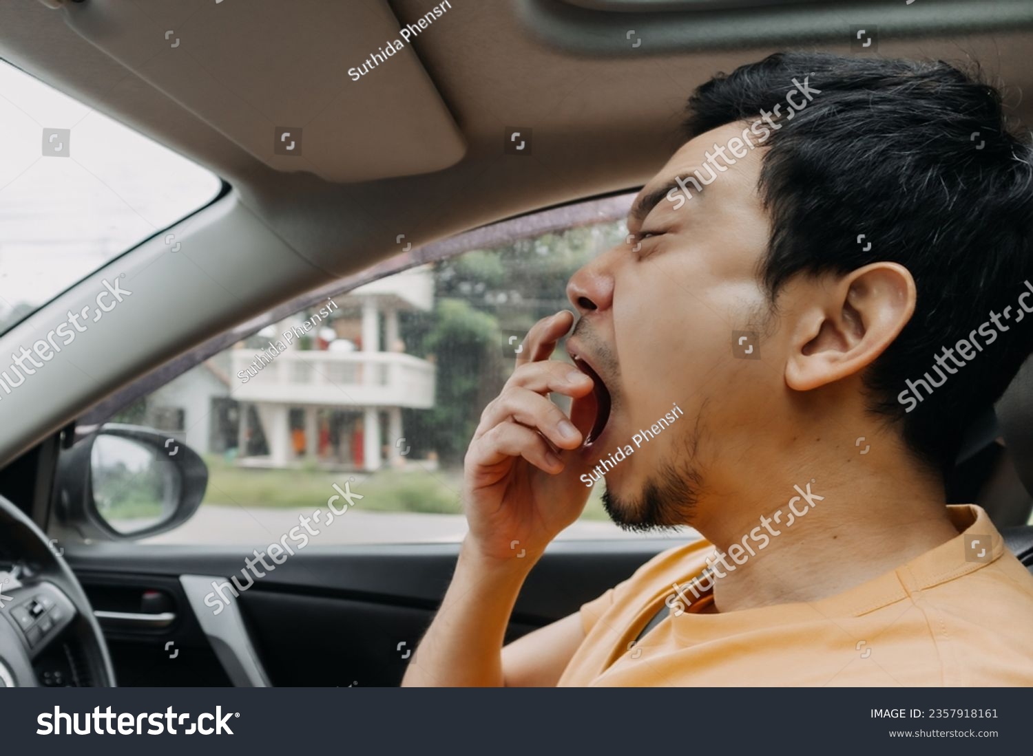 Asian man funny face yawning sleepy while driving a car.  #2357918161