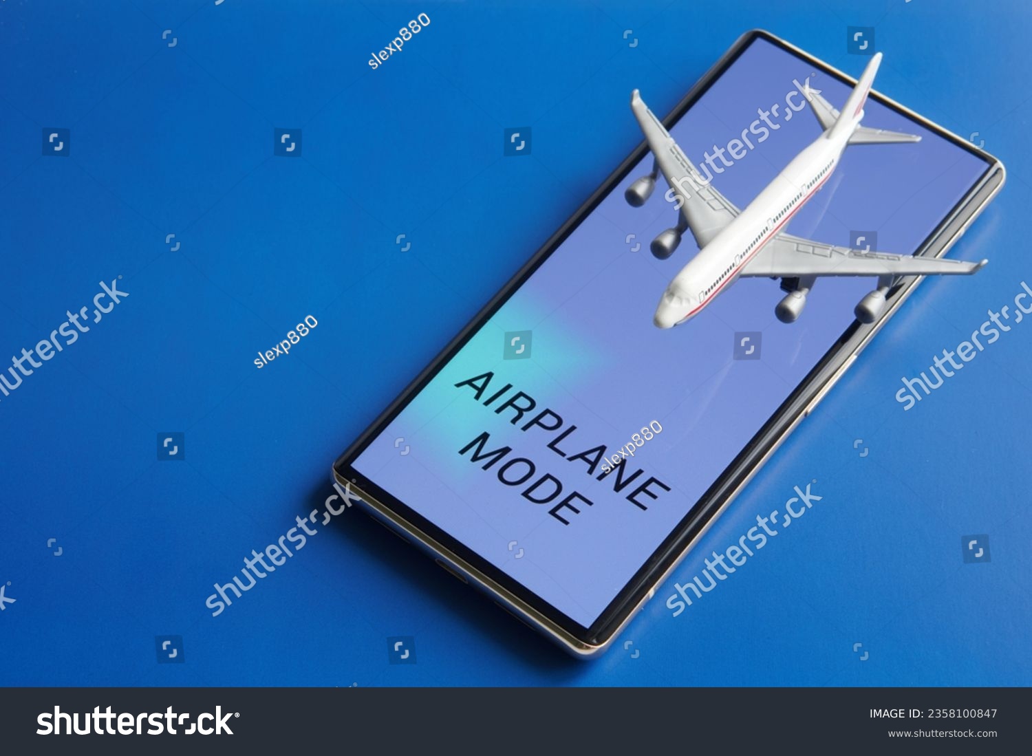 Mobile phone - smartphone with the inscription "Airplane mode" and toy passenger plane. Blue background. Disabling the communication functions of gadgets during an airplane flight. Photo. Close-up #2358100847