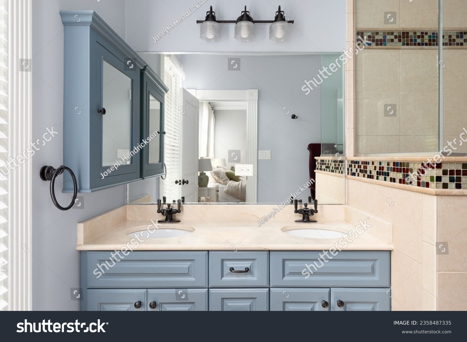 A bathroom with blue cabinet and medicine cabinet, a marble countertop, tiled shower, and view towards the primary bedroom. #2358487335