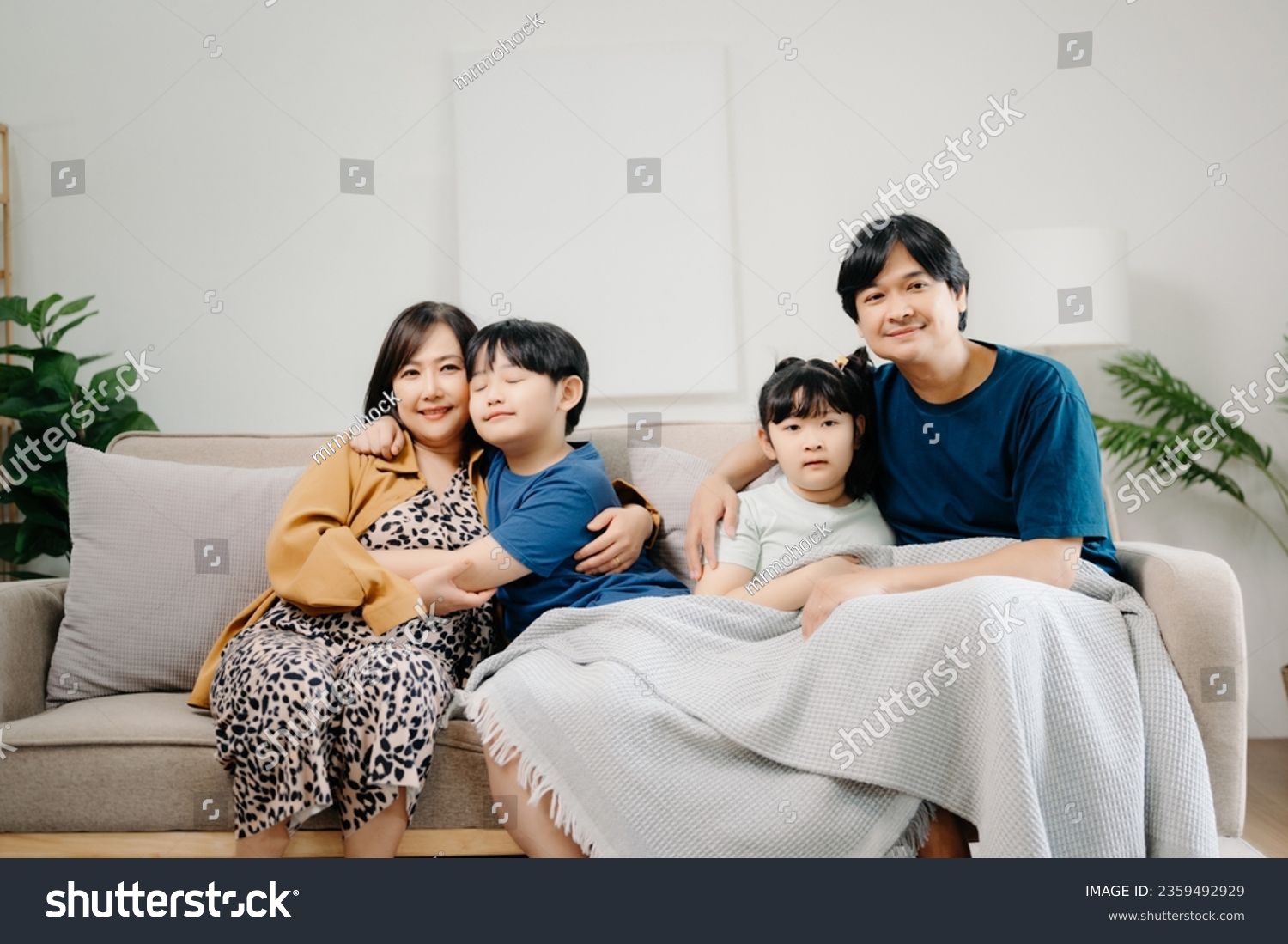 Asian Overjoyed kids sitting on sofa with cheerful parents, watching funny video on computer. Happy married couple enjoying spending weekend time with children, looking at laptop and tablet  #2359492929