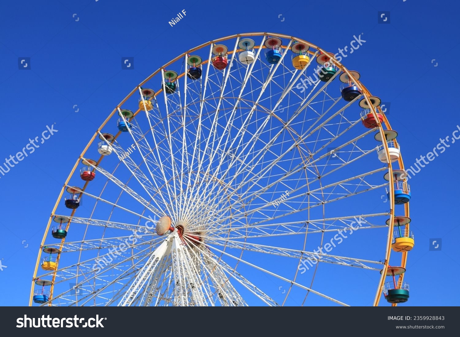 Ferris wheel featuring colourful seating pods against backdrop of blue sky #2359928843