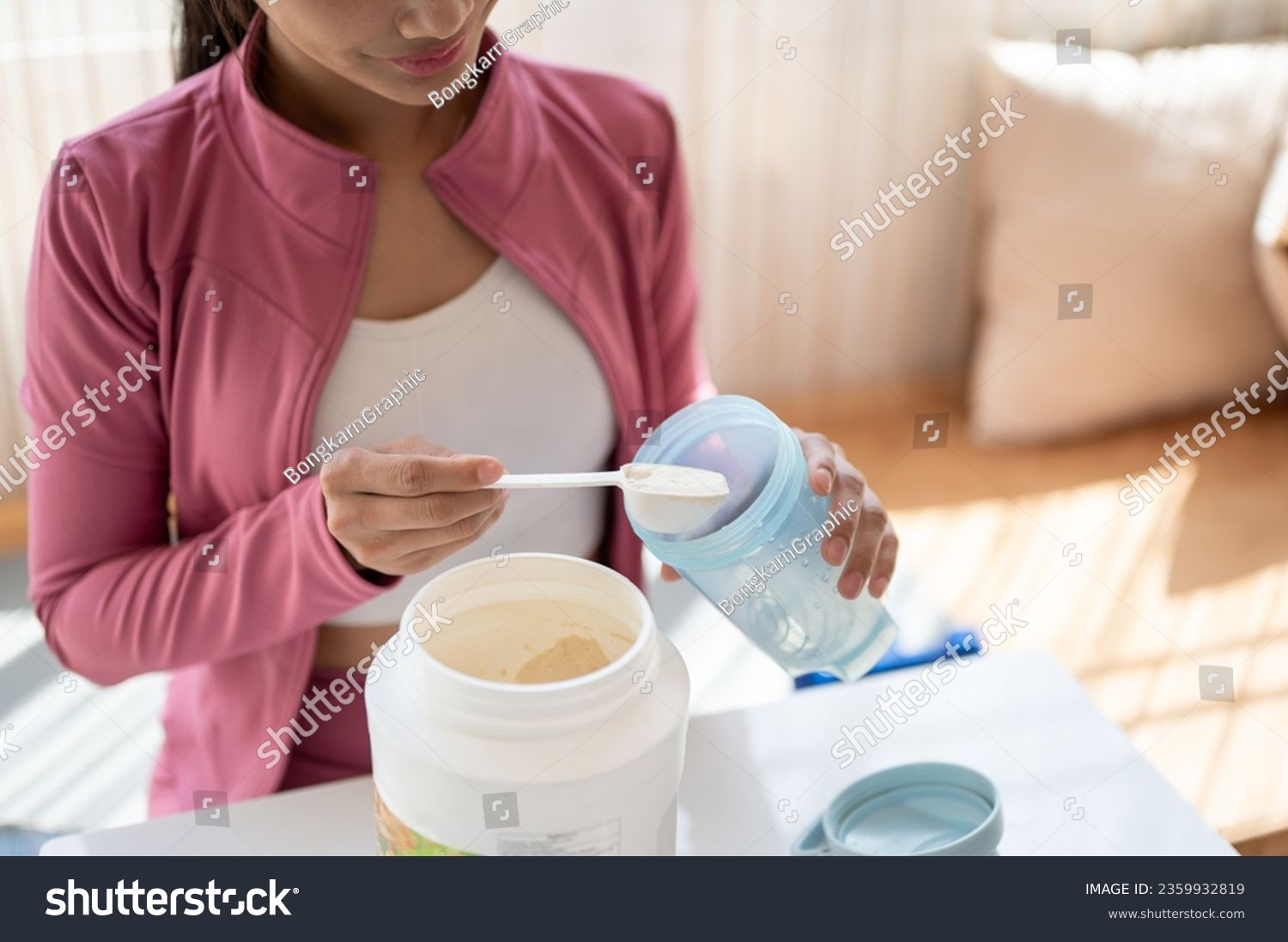 Close-up image of a healthy and fit Asian woman in sportswear making her protein shake after a workout at home. Drink supplements, high-nutrition drinks, diet, and muscle-building #2359932819