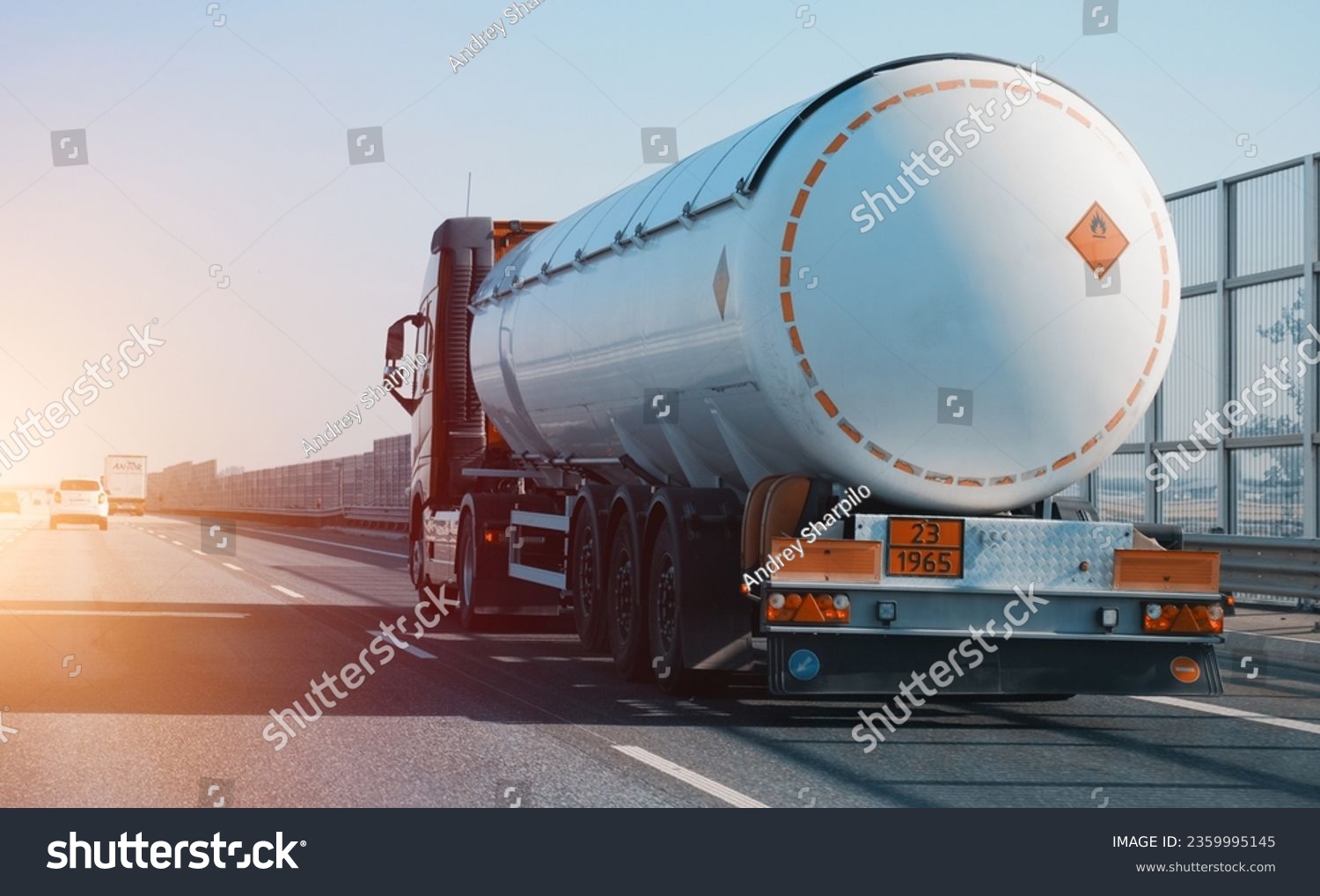 Petrol cargo truck driving on highway hauling oil products. Fuel delivery transportation and logistics concept on a sunny summer evening. Compressed gas carrier truck rear view on a highway. #2359995145