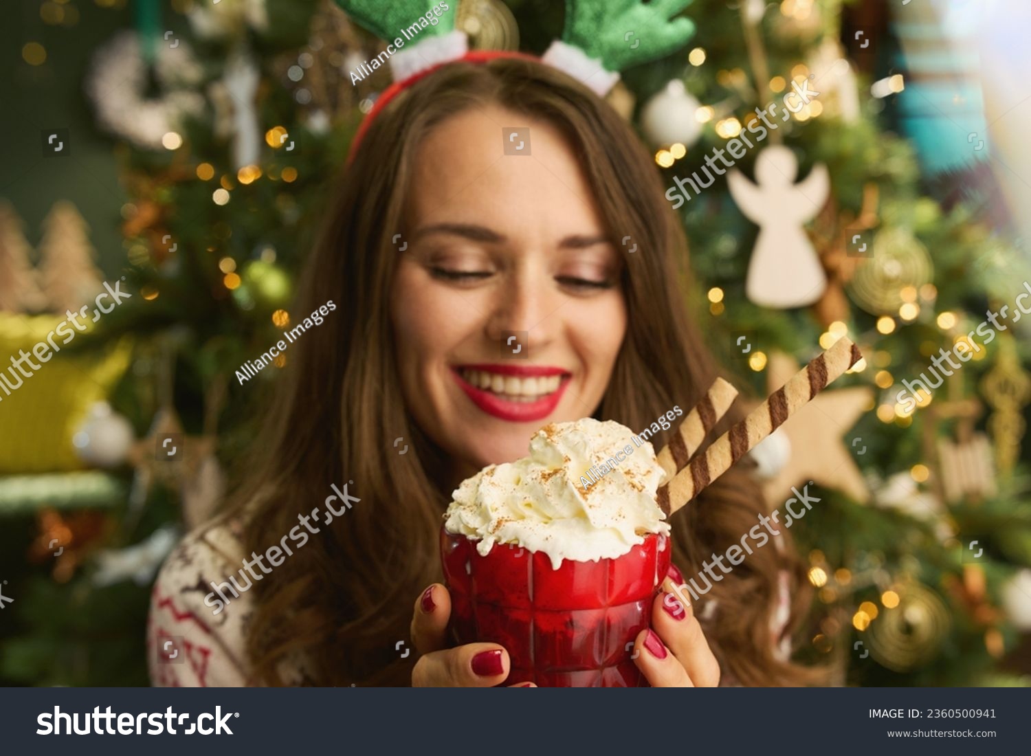 Christmas time. smiling stylish 40 years old housewife with festive hot chocolate cocktail in traditional Christmas sweater near Christmas tree at modern home. #2360500941