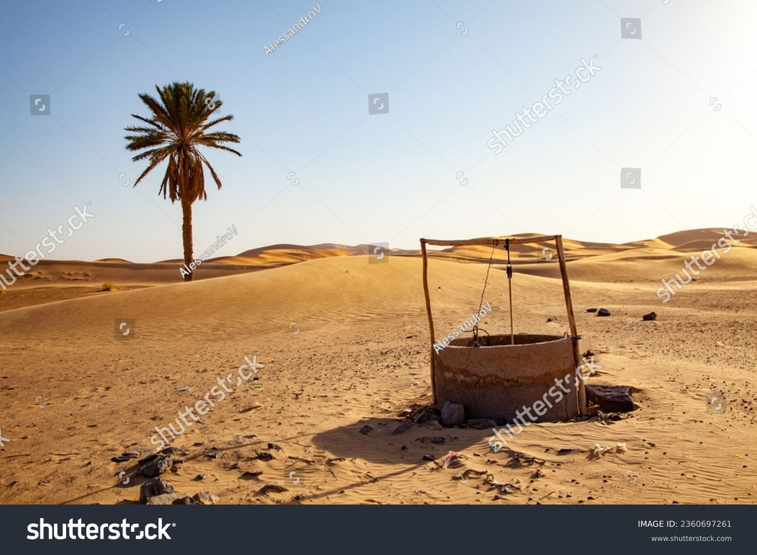 Old water well in the desert with palm tree and dunes in the background #2360697261