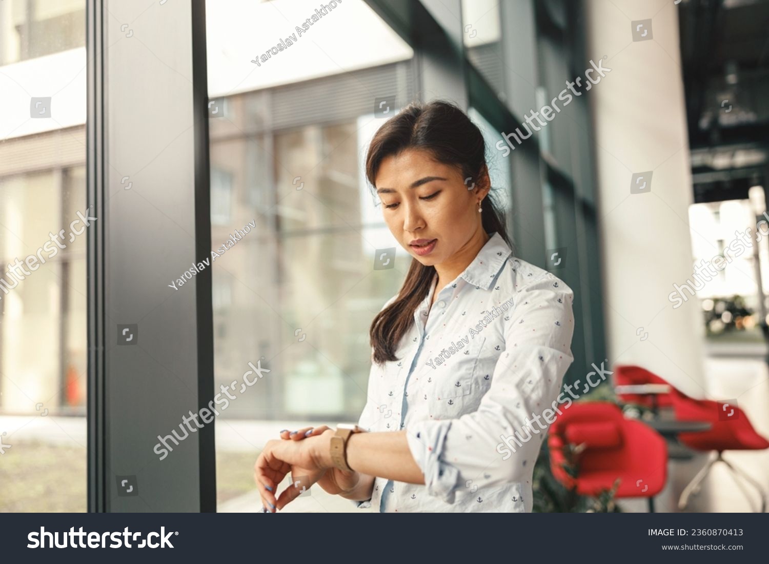 Businesswoman looking on her wrist watch while standing near office window. High quality photo #2360870413