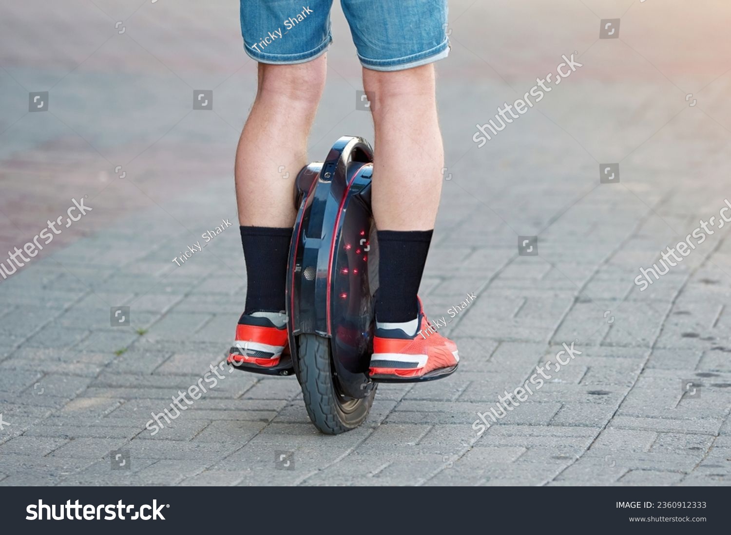 Electric unicycle (EUC), personal mobility. Man in shorts rides on electric mono wheel down the city street in summer season. Man cycling on monowheel. Boy travel on mono wheel.  #2360912333