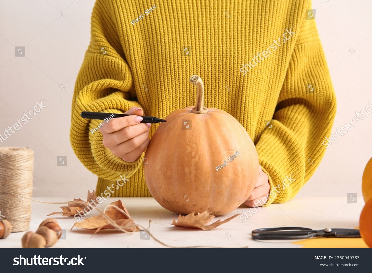 Woman painting pumpkin for Halloween celebration on light background #2360949783