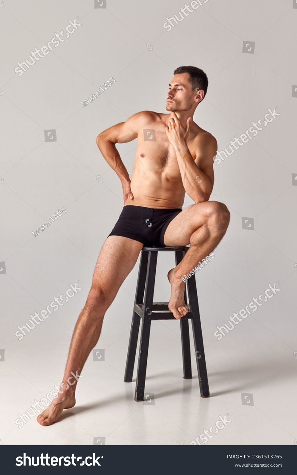 Full-length portrait of handsome, muscular young man sitting on chair in underwear and posing against grey studio background. Concept of men's health and beauty, body care, fitness, wellness, ad #2361513265