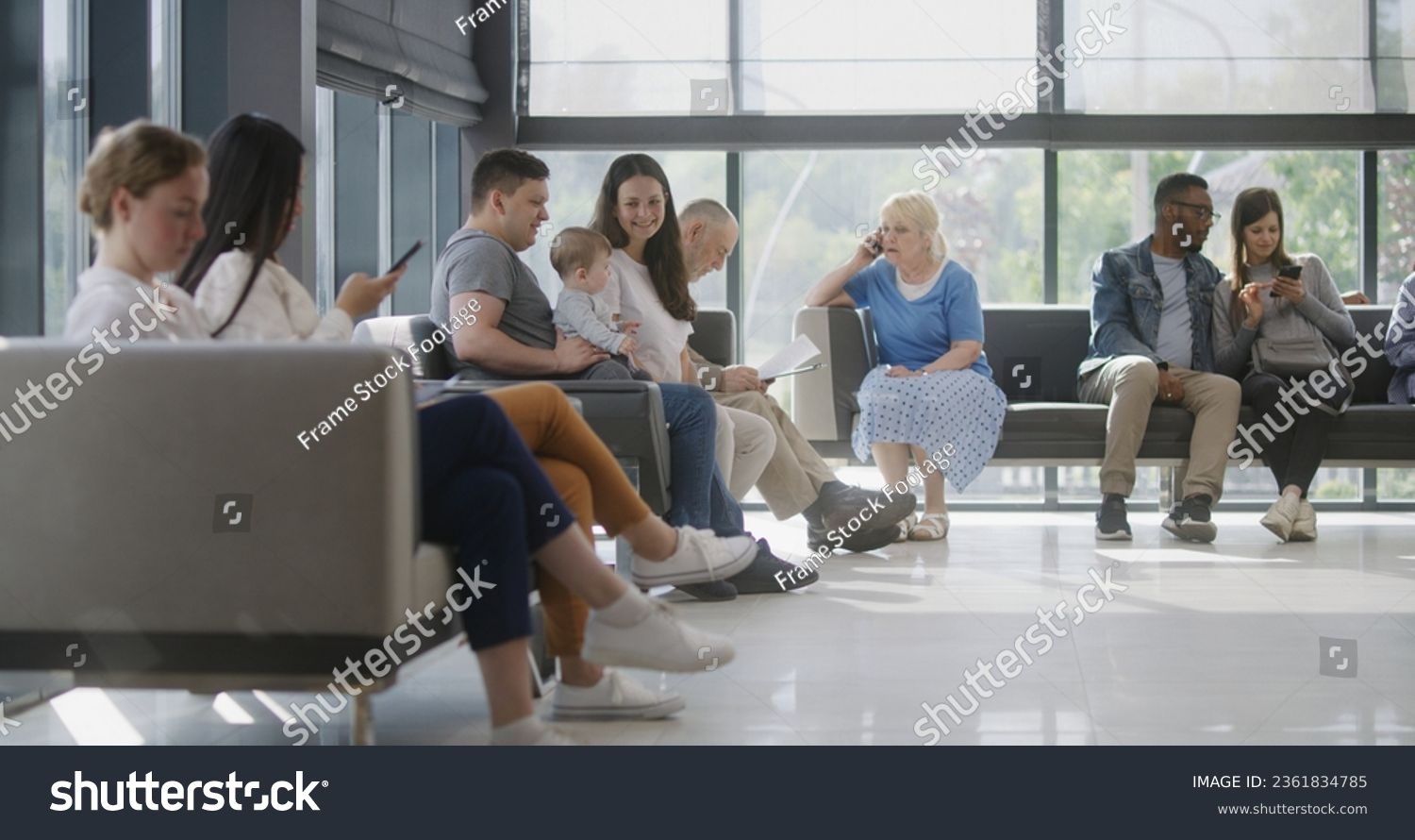 Diverse multicultural people sit on couches in clinic lobby area, wait for appointment with doctor or medical test results. Waiting area in medical center with modern design. Healthcare system. #2361834785