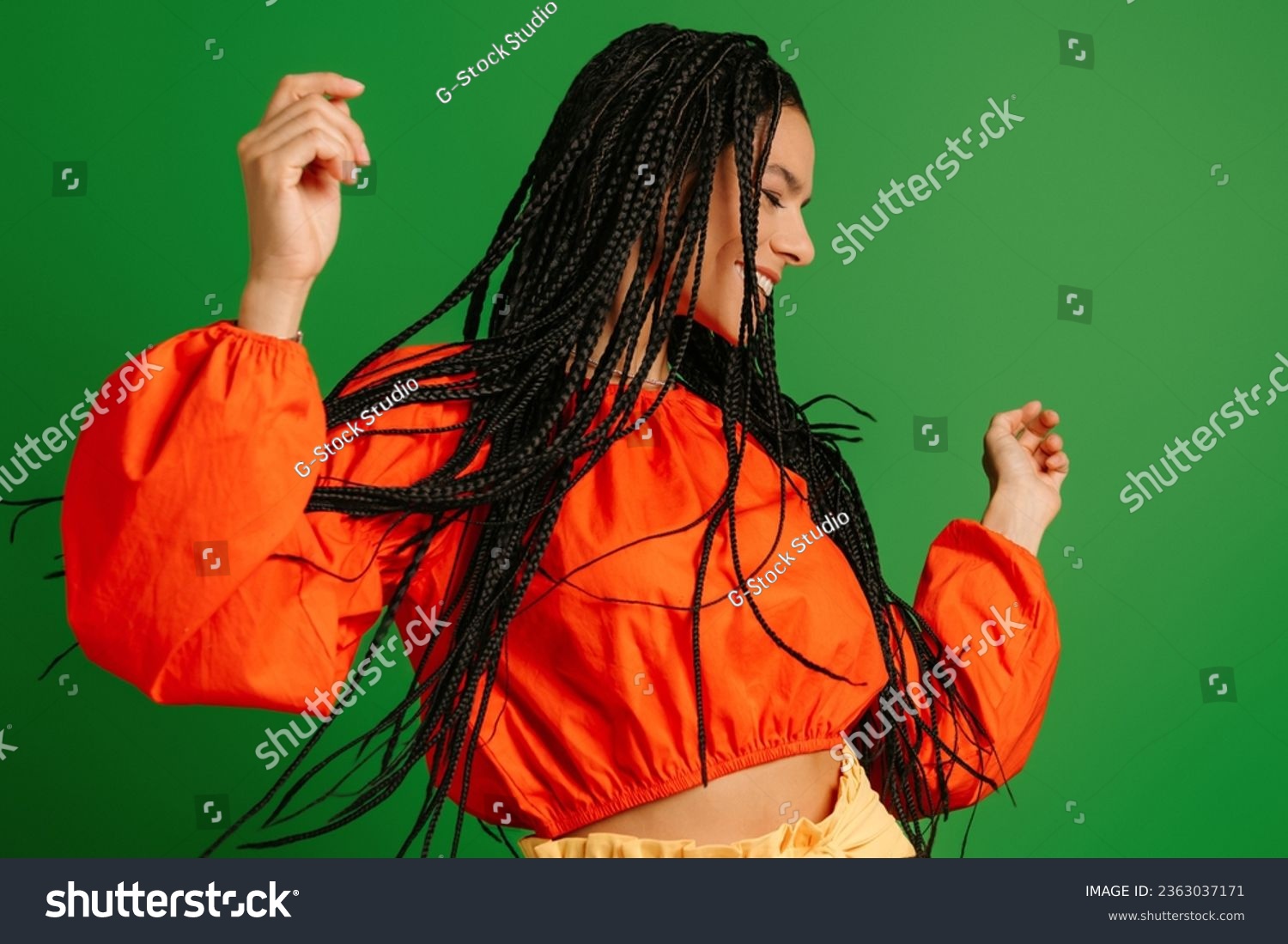 Happy young woman with dreadlocs dancing and smiling against green background #2363037171