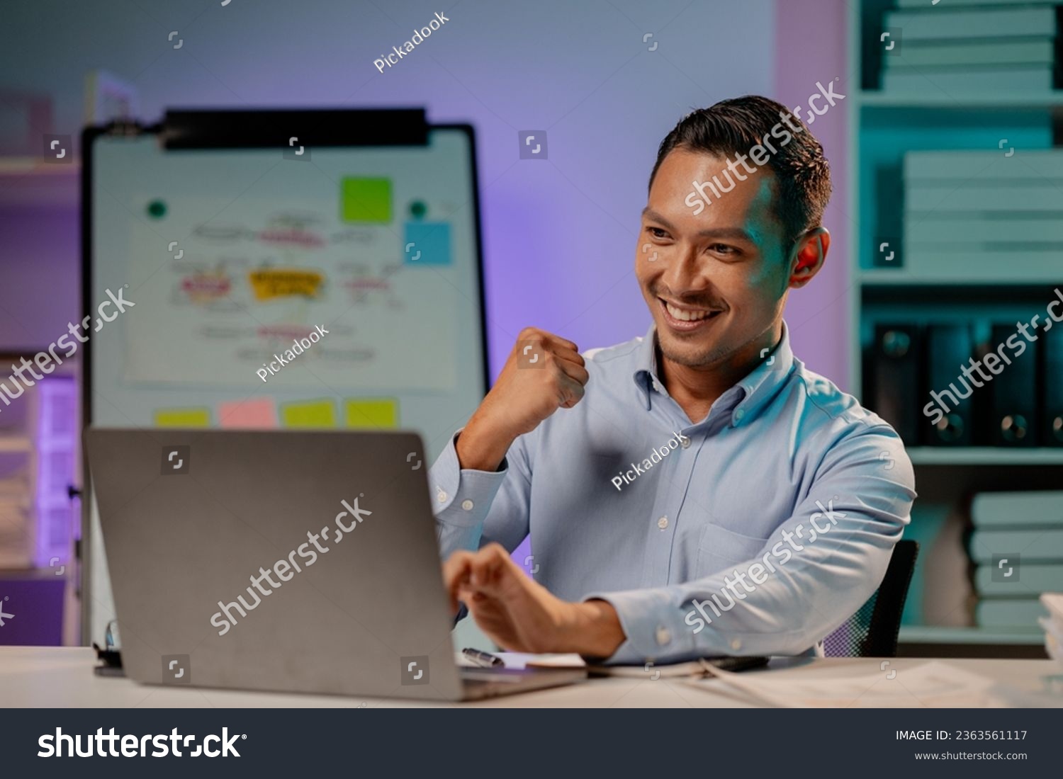 Asian man showing happy expression in the office, company employee working overtime, working late at night, working overtime of a busy and hardworking company employee. Overtime concept. #2363561117