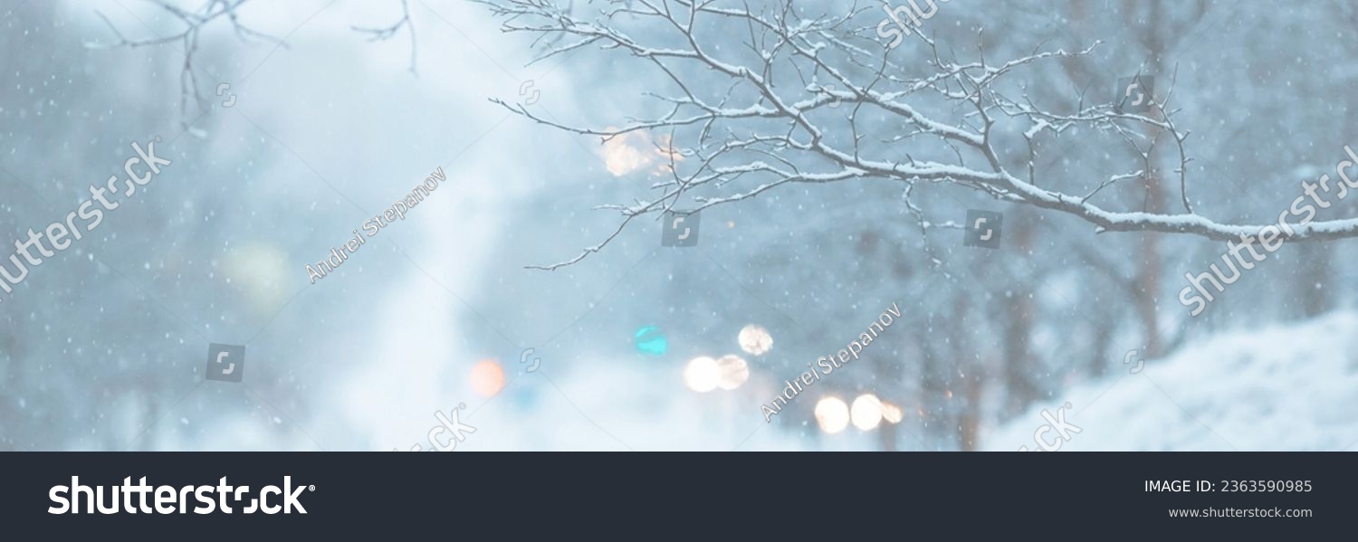 Snow-covered branches and snowflakes in the air. Glittering lights out of focus. Cold winter snowy weather. Evening twilight. Shallow depth of field and blurry background. Wide panoramic background. #2363590985