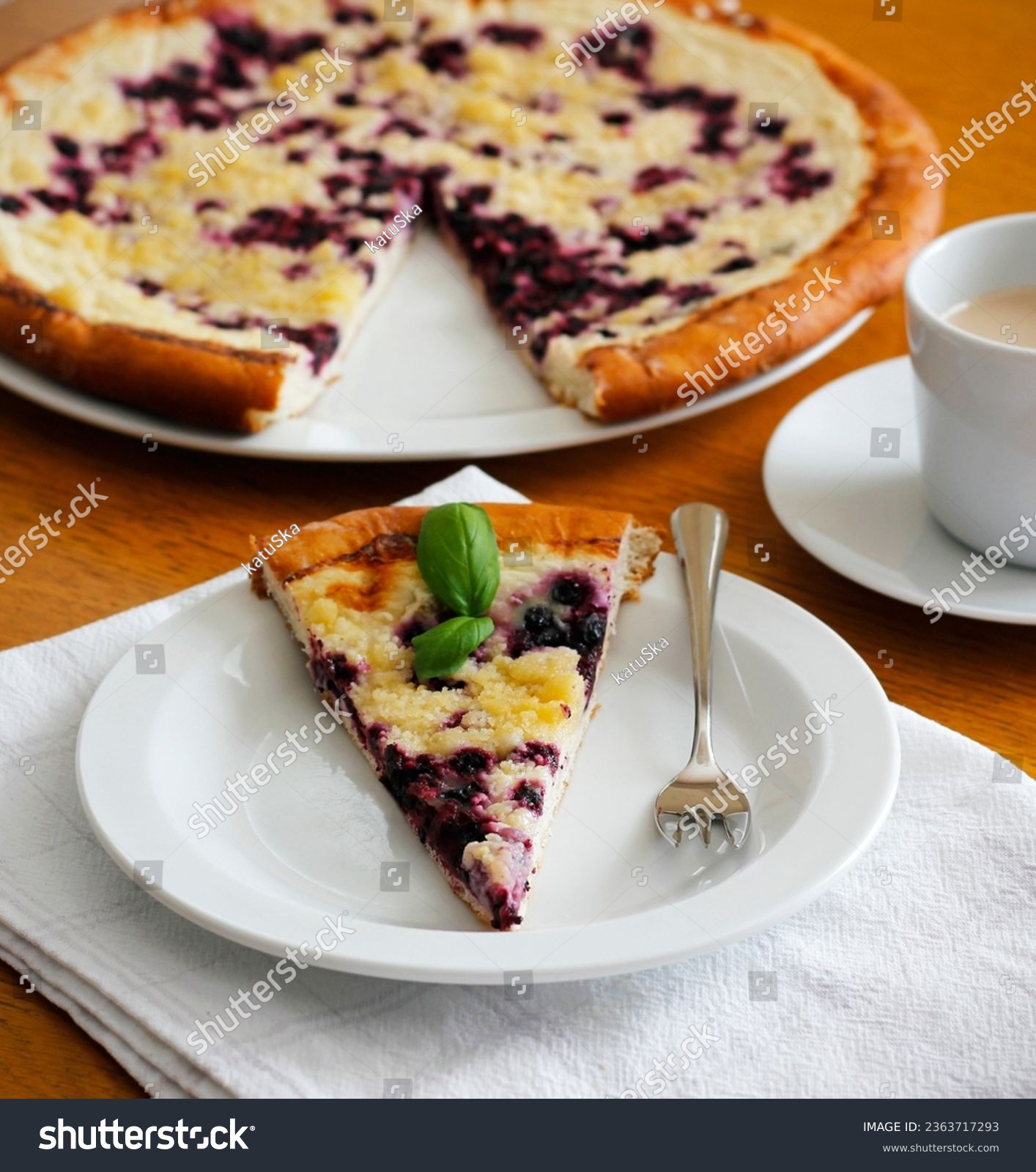 Piece of traditional Wallachian blueberry pie called "frgal" on a white plate. Traditional Moravian sweet dessert on wooden table. Typical Czech cuisine concept. Summer fruit cake. Selective focus. #2363717293