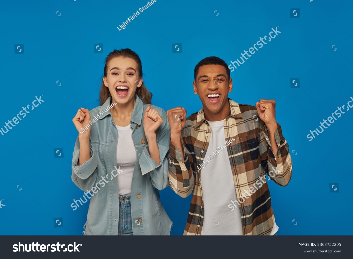 excited interracial couple screaming from joy looking at camera on blue backdrop, emotional reaction #2363752205