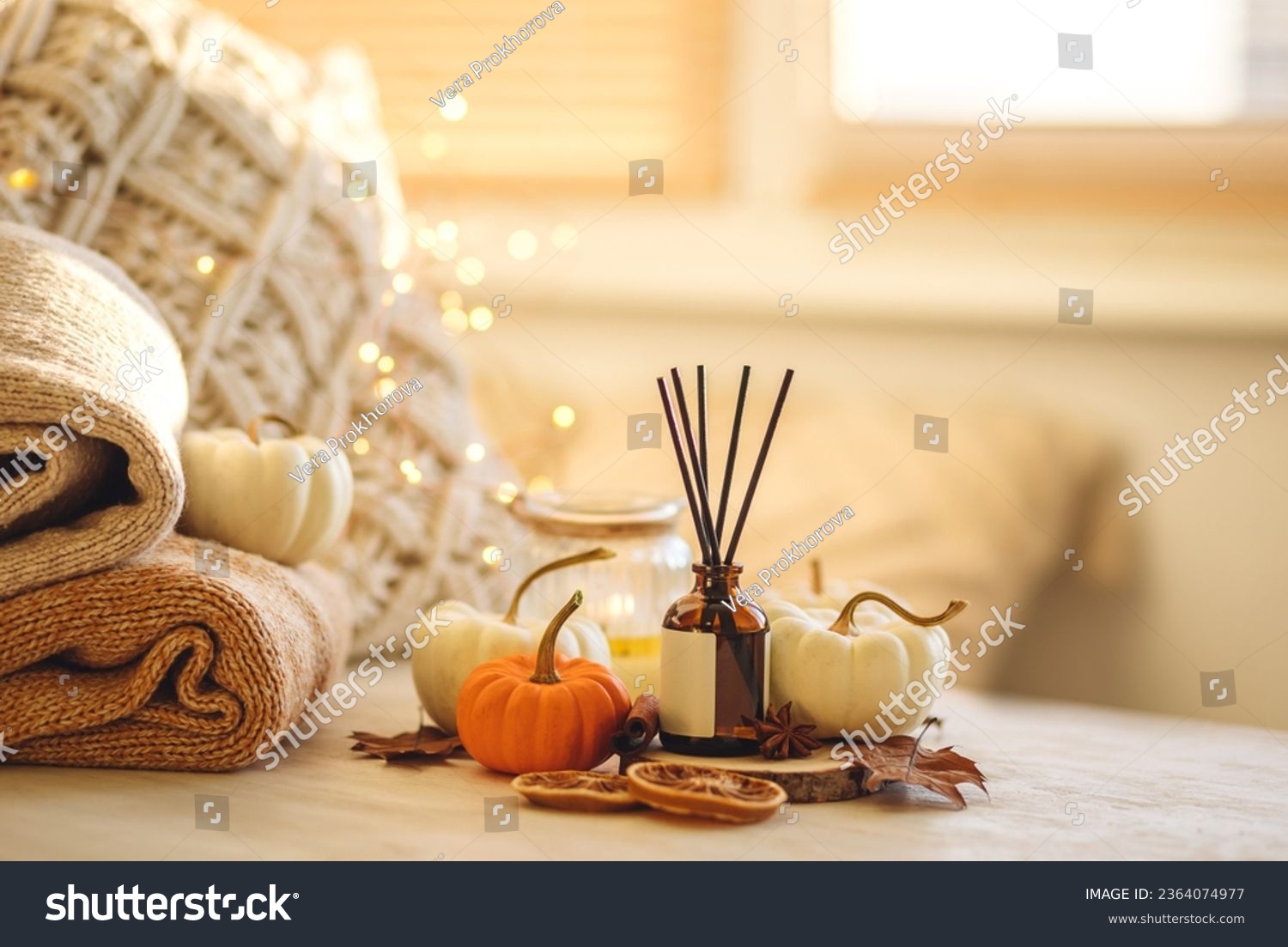 Autumn mood, cozy fall home atmosphere. Aroma diffuser, pumpkins, knitted warm sweaters, burning candles, dry leaves on wooden table. Concept of house decor, apartment seasonal fragrance. Thanksgiving #2364074977