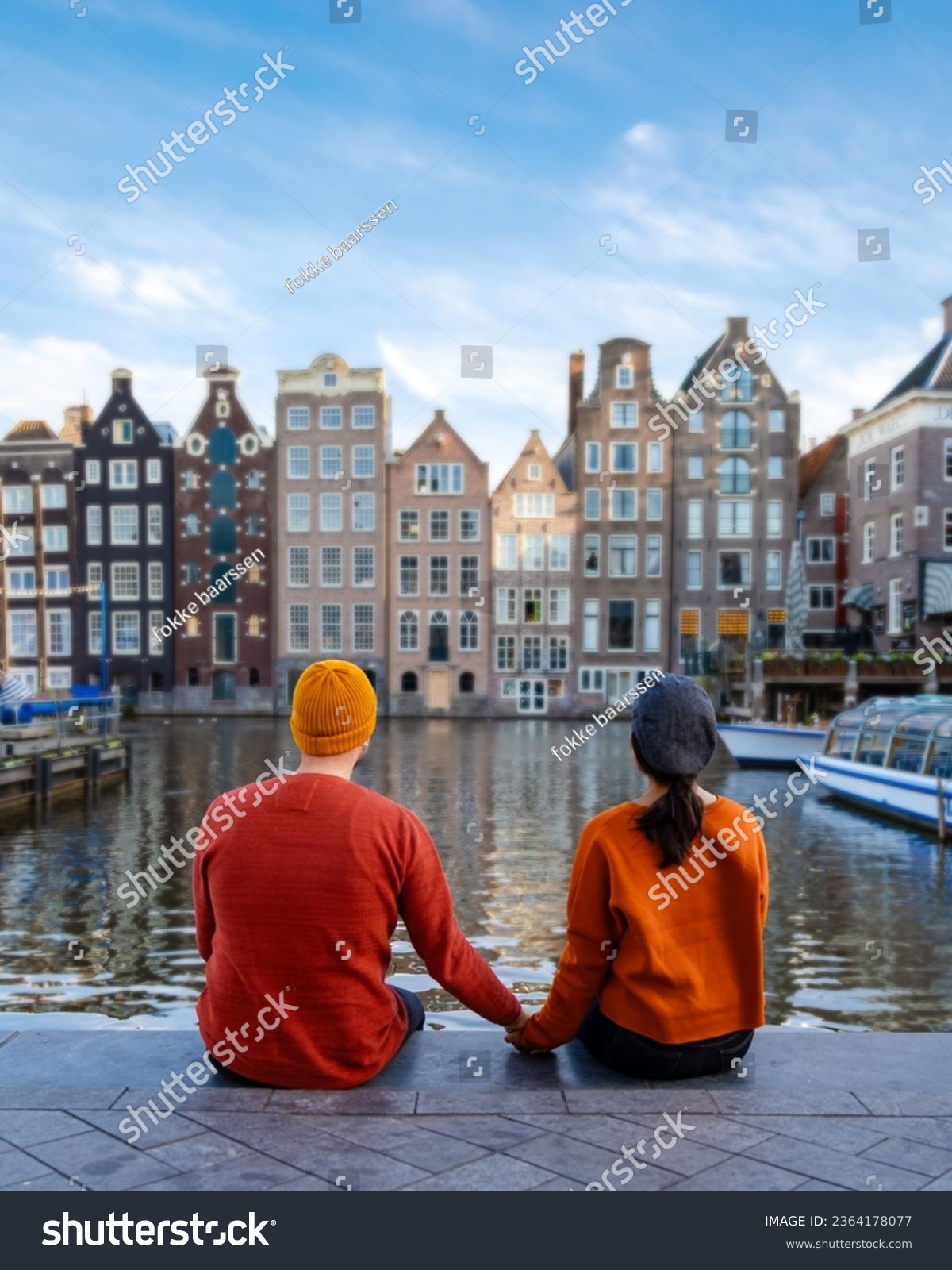  a couple of men and a woman visit the city of Amsterdam with orange colors alongside the canal men and women mid age city trip to Amsterdam #2364178077