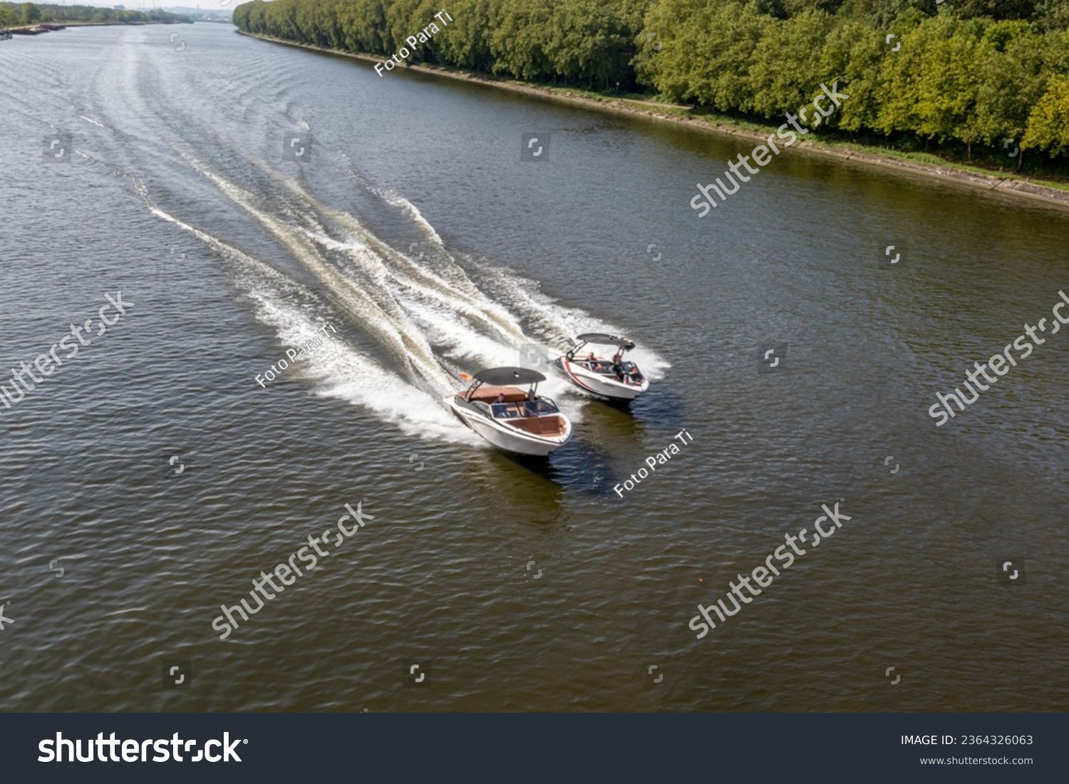 Two small boats sailing at high speed on calm waters along Albert canal, lush green trees, blurry and foggy background, sunny summer day in Liege province, Belgium #2364326063
