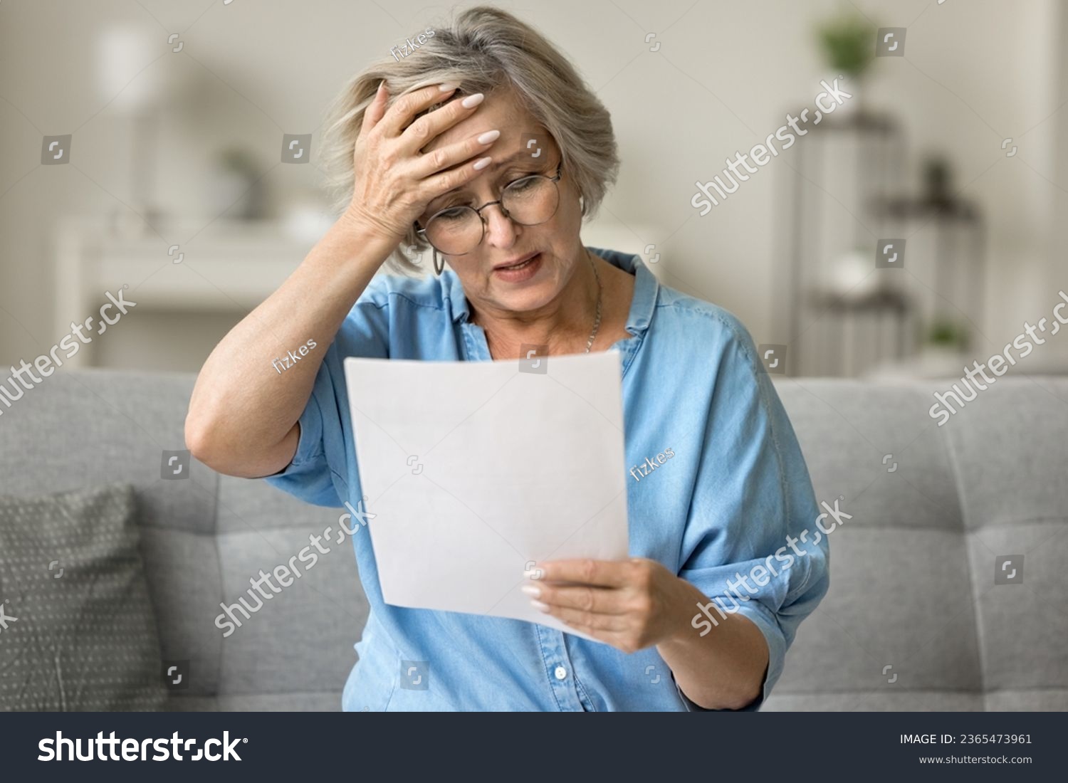 Stressed frustrated older woman getting bad news from paper letter, reading document at home, touching head in despair, panic attack, sitting on couch, receiving concerning medical result #2365473961