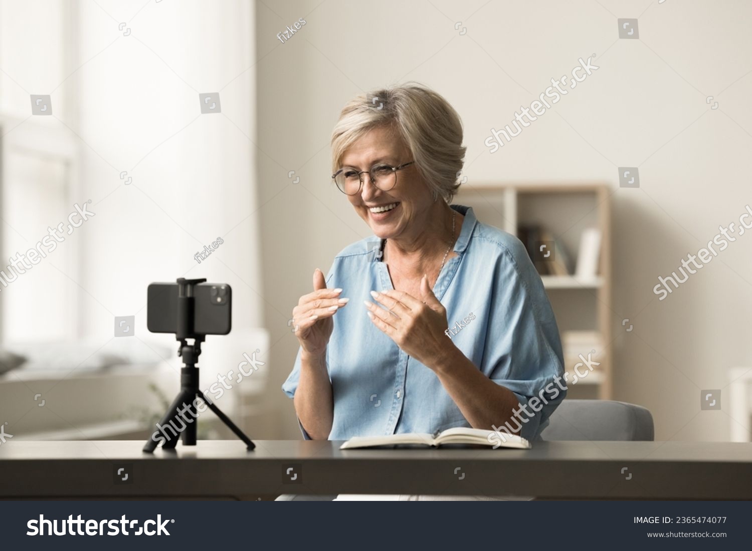 Cheerful senior elder influencer woman working on shooting for blog, recording selfie video at home, speaking at cellphone camera fixed on tripod, smiling, broadcasting online #2365474077