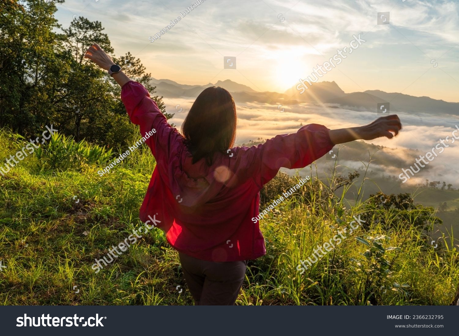 Female tourists carry backpacks, travel, hike, watch the mist as the sun rises to the top of the mountain, and relax, stretching their arms, feeling free in the morning, weekend holidays. #2366232795
