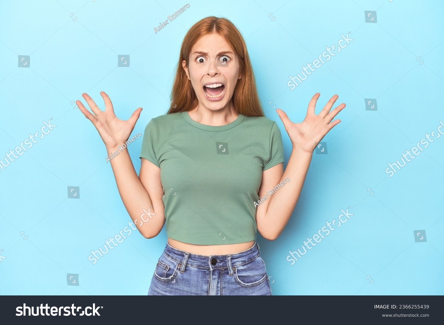 Redhead young woman on blue background screaming to the sky, looking up, frustrated. #2366255439