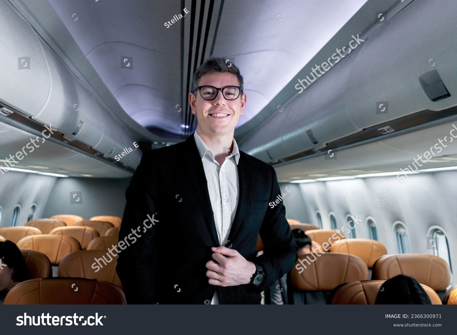 Portrait of happy smiling businessman in black suit, standing on aisle inside airplane, male passenger traveling on business trip by aircraft, businesspeople traveling with airline transportation. #2366300971