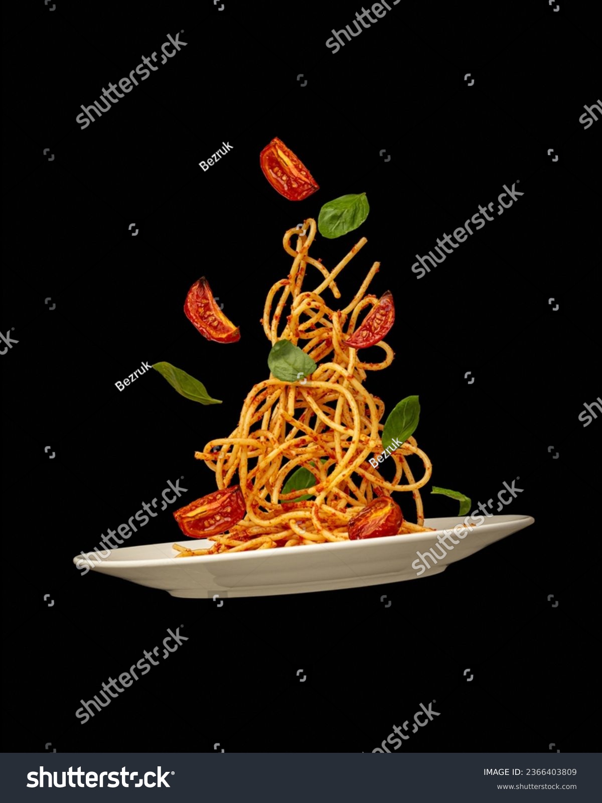 Pasta falling into a plate with tomatoes and basil on a black background. Levitation #2366403809