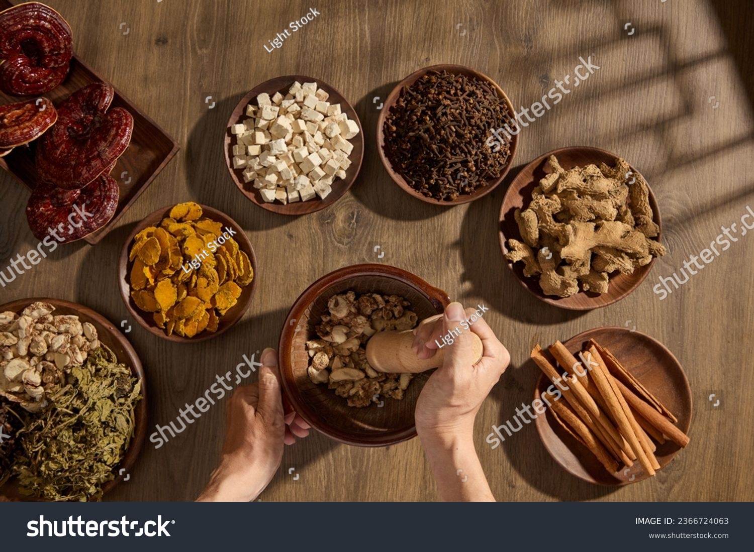 Scene of traditional medicines on wooden trays, decorated on vintage table background with window shadow. Top view, the apothecary's hand is pounding medicine in a wooden mortar #2366724063