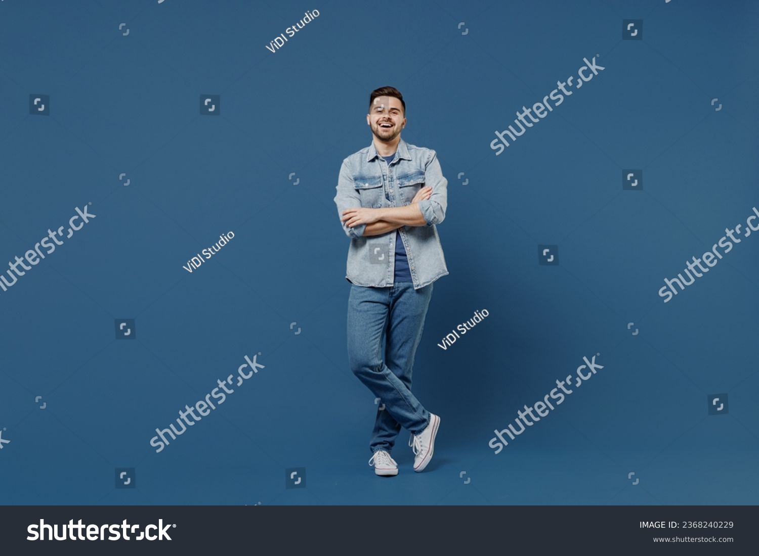 Full size length body laughing beautiful happy handsome young brunet man 20s wears denim jacket hold hands crossed isolated on dark blue background studio portrait. People emotions lifestyle concept. #2368240229