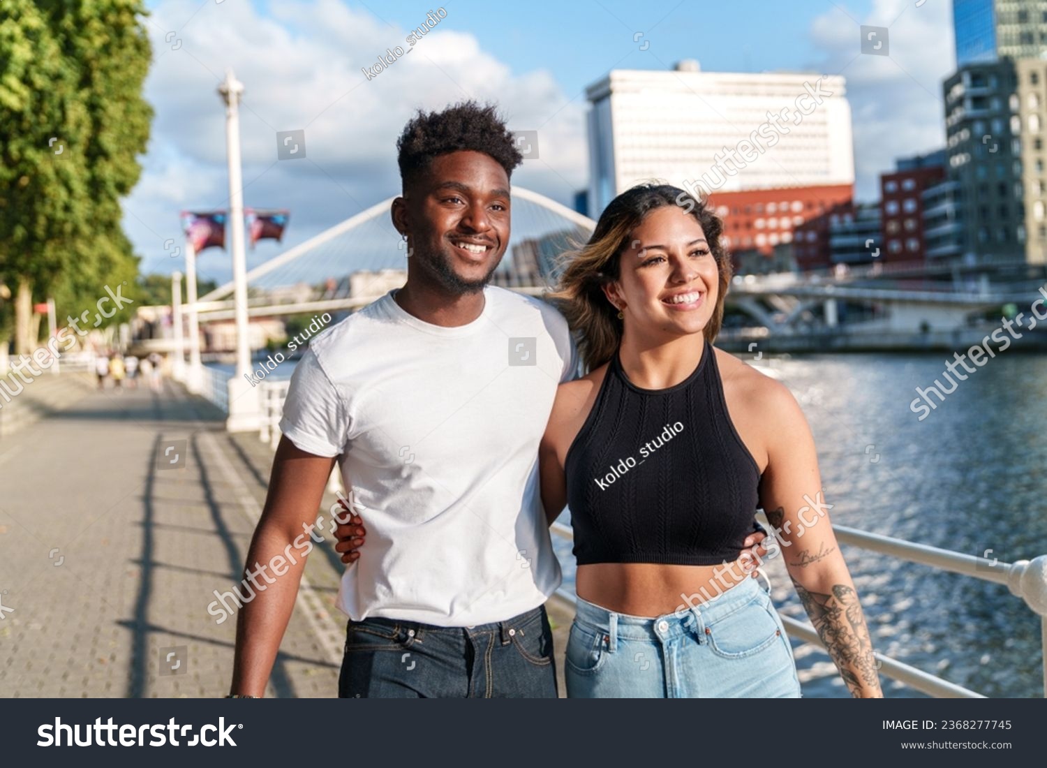A colorful, urban evening by the riverside with two attractive, diverse models in casual attire, radiating joy. #2368277745
