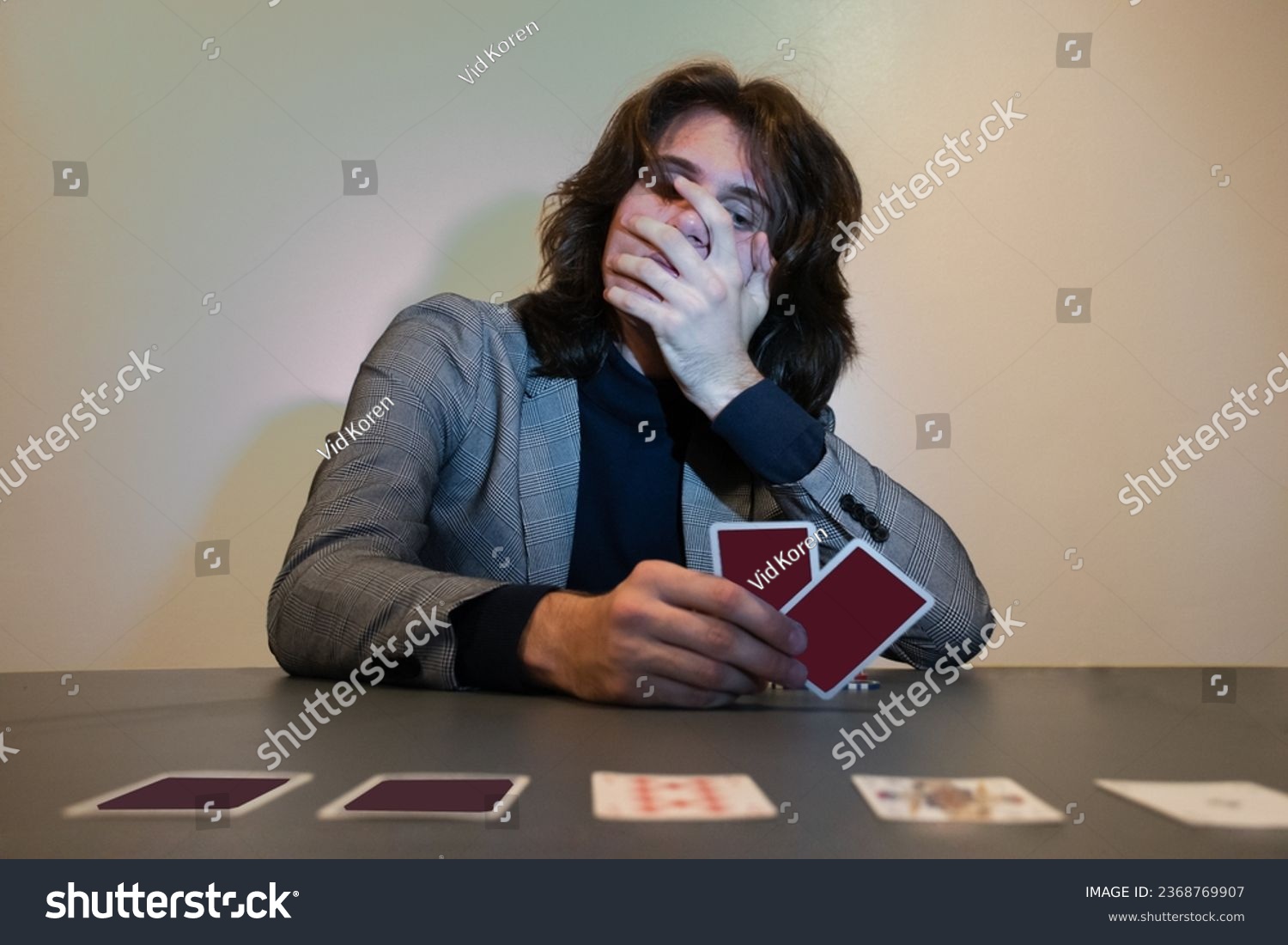 Man in a suit playing poker - card game and holding his mouth while holding his playing cards. Surprised, sad, gambling addiction concept. #2368769907