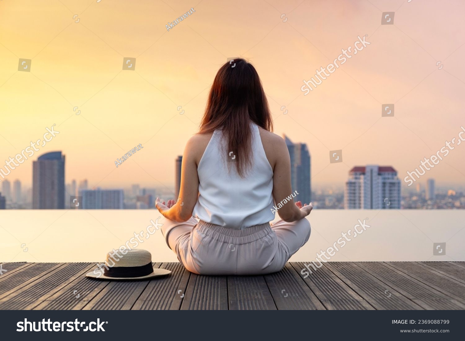 Back of woman relaxingly practicing meditation at the swimming pool rooftop with view of urban skyline building to attain happiness from inner peace wisdom #2369088799