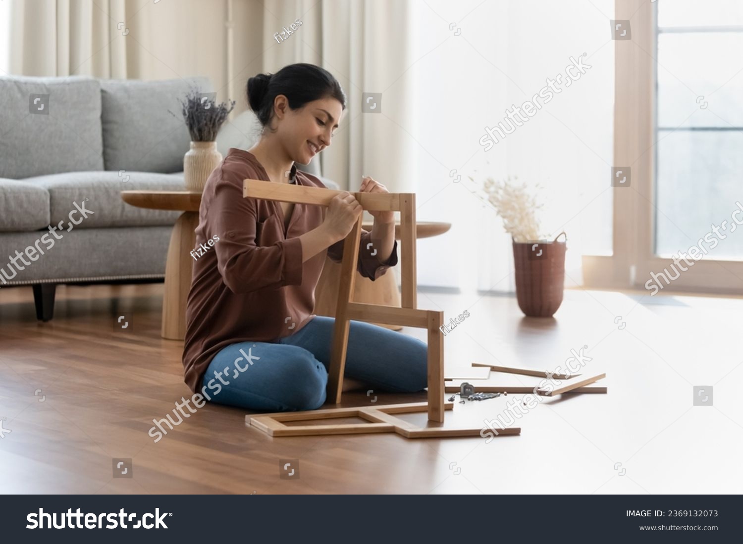 Smiling Indian woman assembling new wooden furniture, sitting on floor in living room at home, happy young female renter customer putting wooden shelf or chair pieces together, renovation concept #2369132073