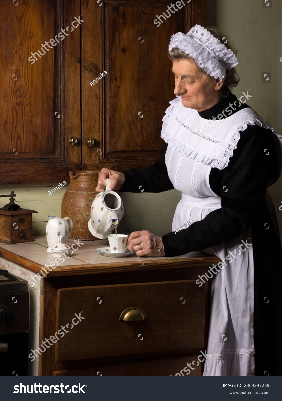 Victorian maid or servant in black dress, lace cap and white apron working in a 19th century interior #2369297289