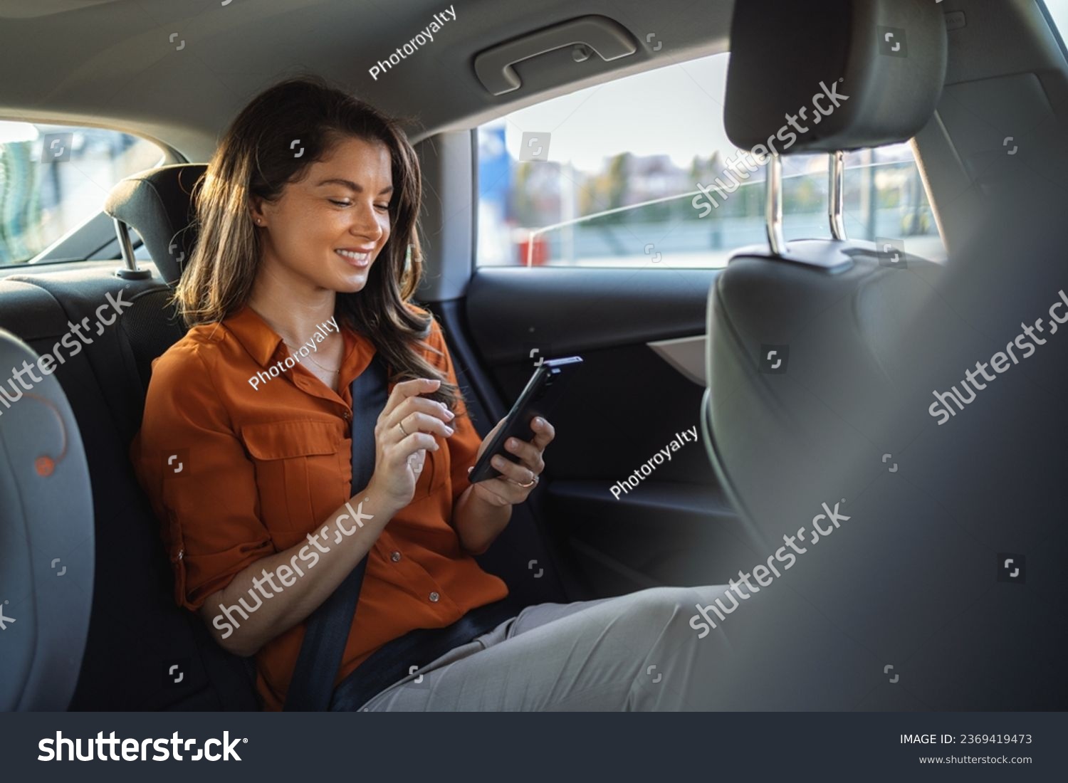 Beautiful Businesswoman is Commuting from Office in a Backseat of Her Luxury Car. Entrepreneur Passenger Traveling in a Transfer Taxi in Urban City Street #2369419473