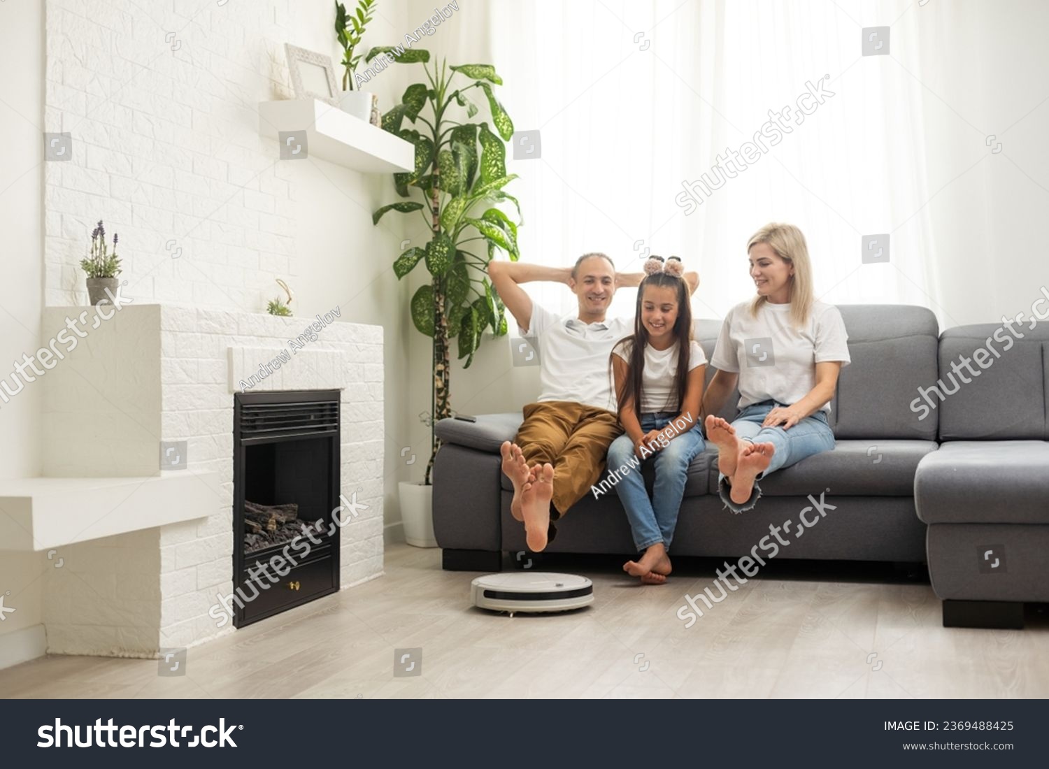Young family resting on the couch while robotic vacuum cleaner doing its work at home. Household robots concept. #2369488425