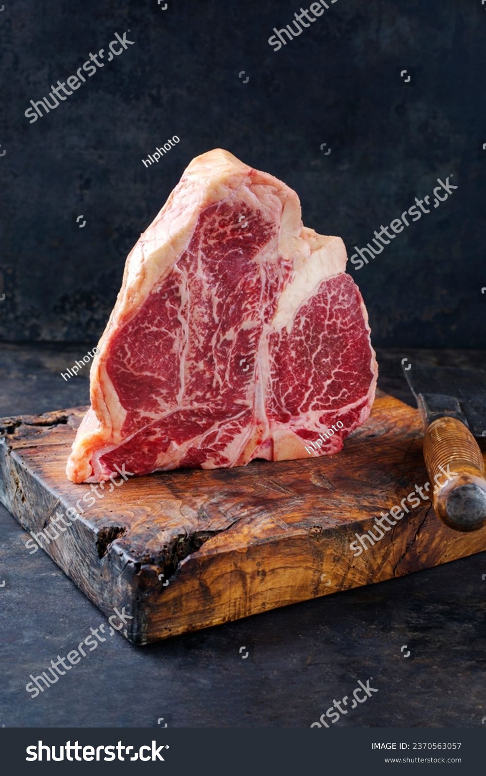Raw dry aged wagyu porterhouse beef steak offered as close-up on rustic old wooden board with a knife  #2370563057