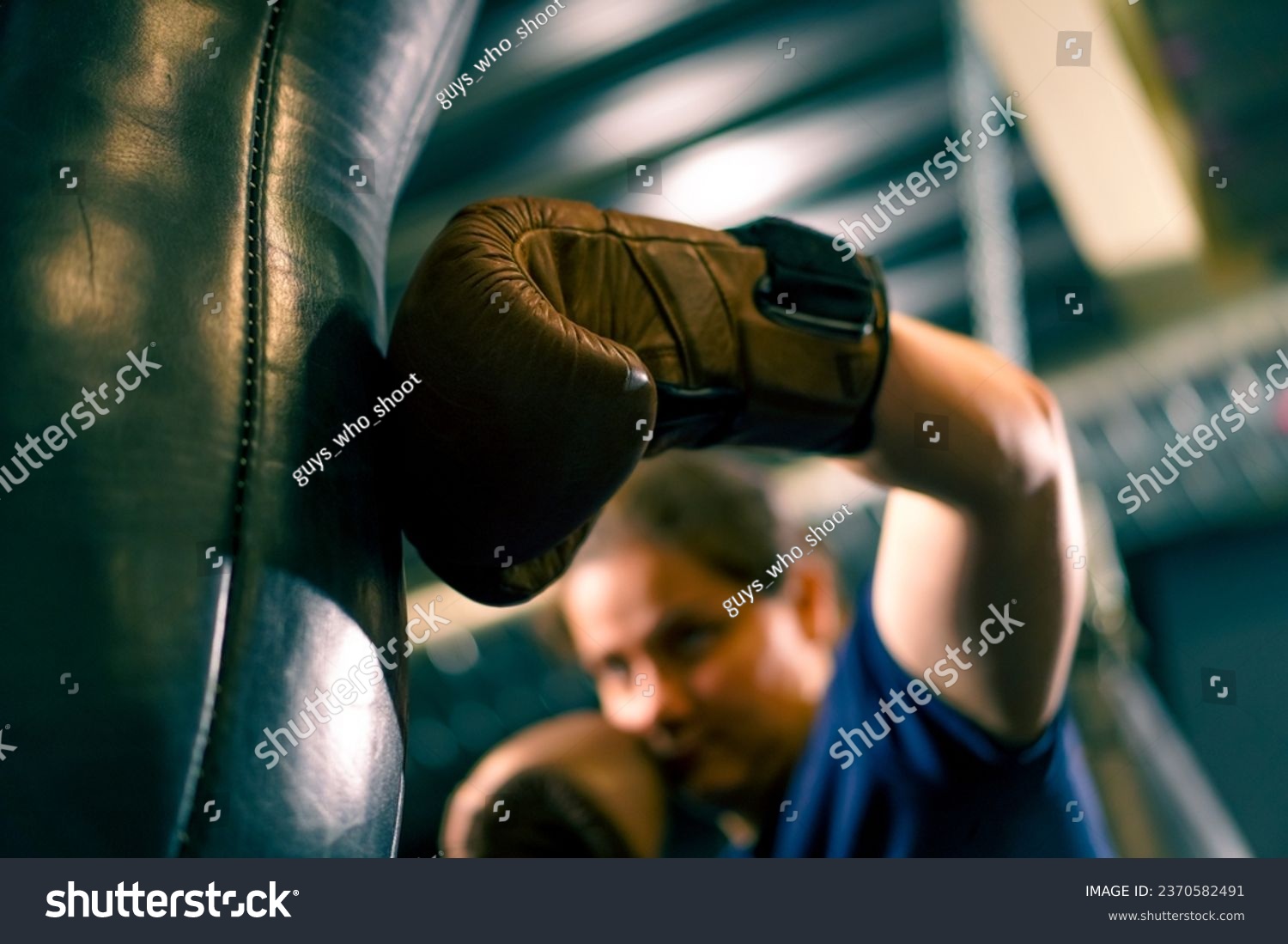 a girl boxer in gloves works out the strength of punches on a punching bag in the gym trains hard before fight close-up #2370582491