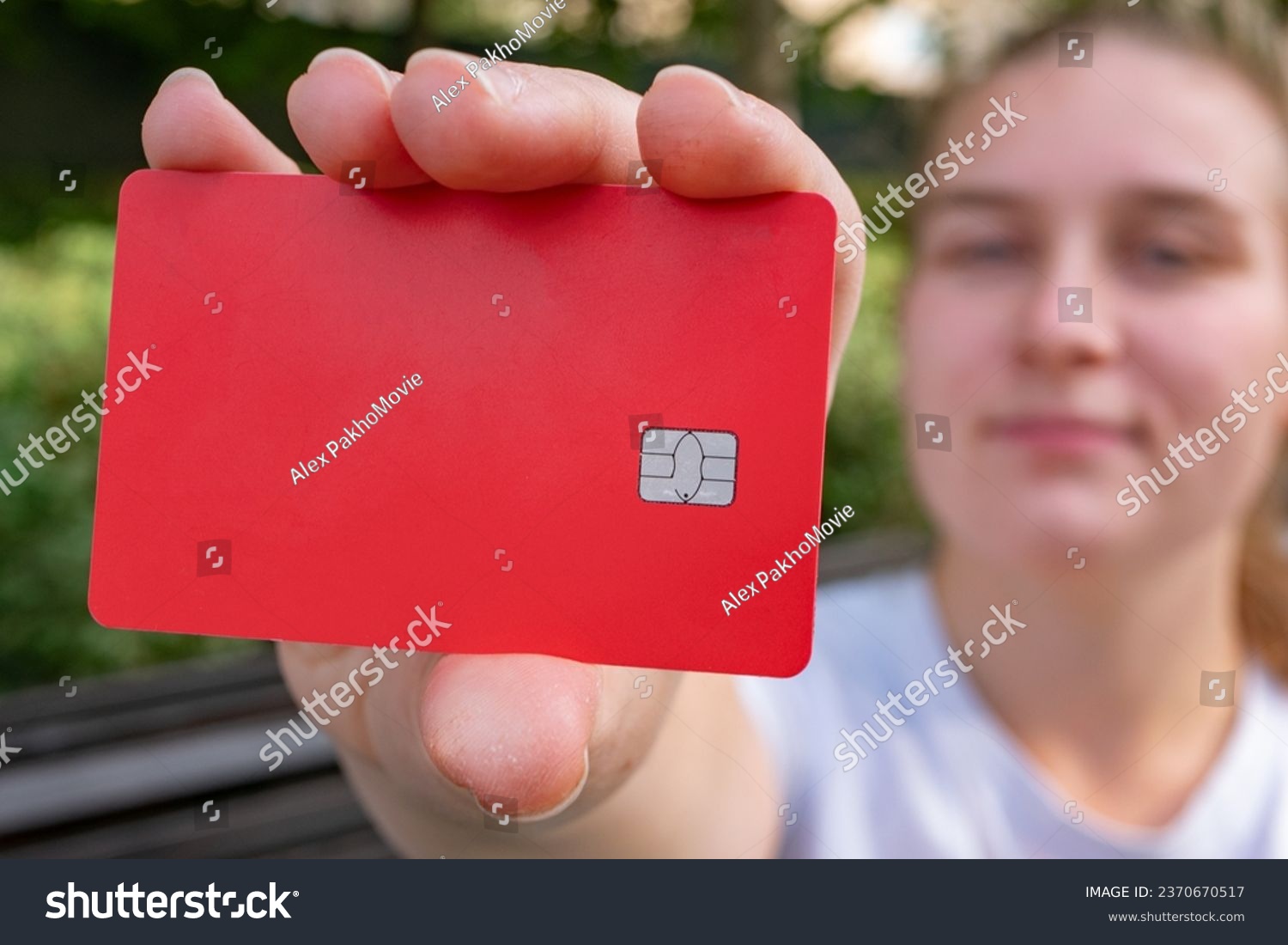 A girl on the street is holding a red credit card with no writing on it. A close-up of a red bank card in her hand. Bank card chip.  #2370670517