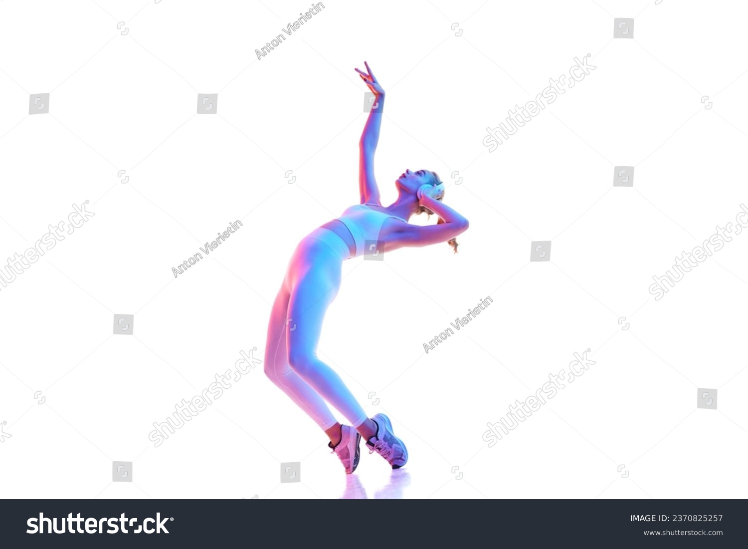 Side view portrait of young slim flexible woman posing with music in headphones isolated white background in neon light. Concept of sport, fitness, healthy lifestyle, strength, youth, ad. Copy space #2370825257