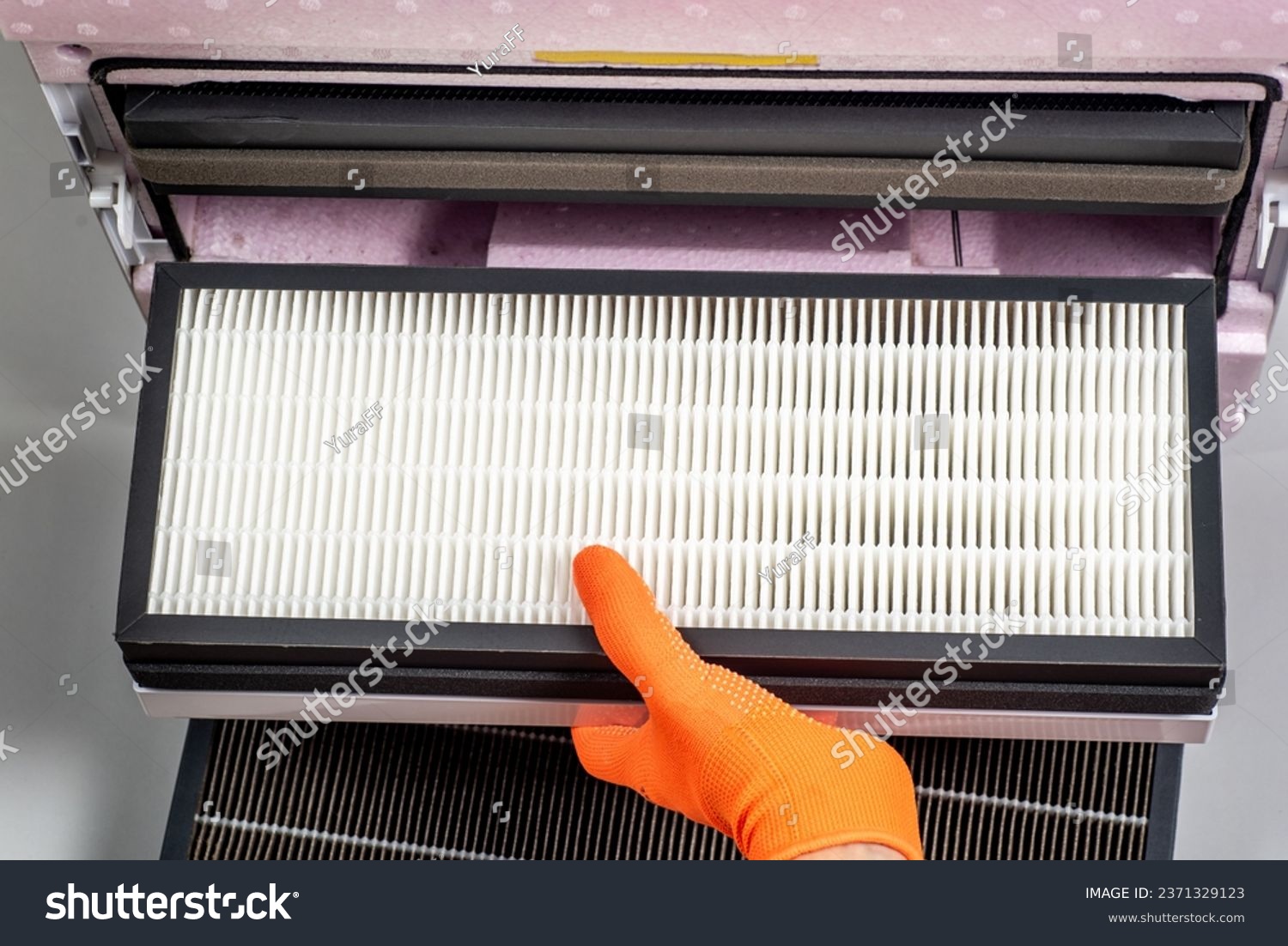 Replacing filters in a home ventilation system. A hand in an orange glove changes a Hepa filter. #2371329123