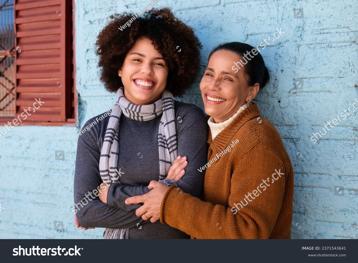 Happy cheerful black adult daughter and mother with broad smile embracing each other outside humble home Togetherness, family, support concept. #2371543641