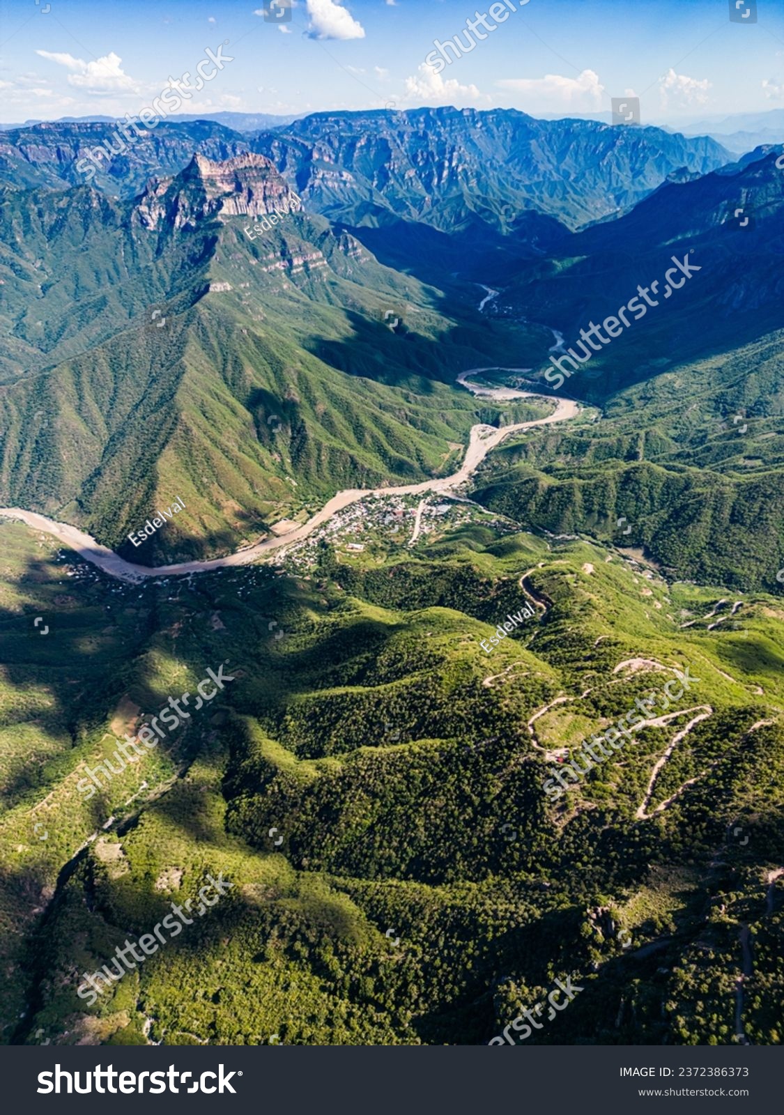 From a drone's eye, the aerial panorama of Urique Canyon within Copper Canyon, Chihuahua unveils a winding road leading to the nestled village of Urique, portraying a scenic narrative of remote charm #2372386373