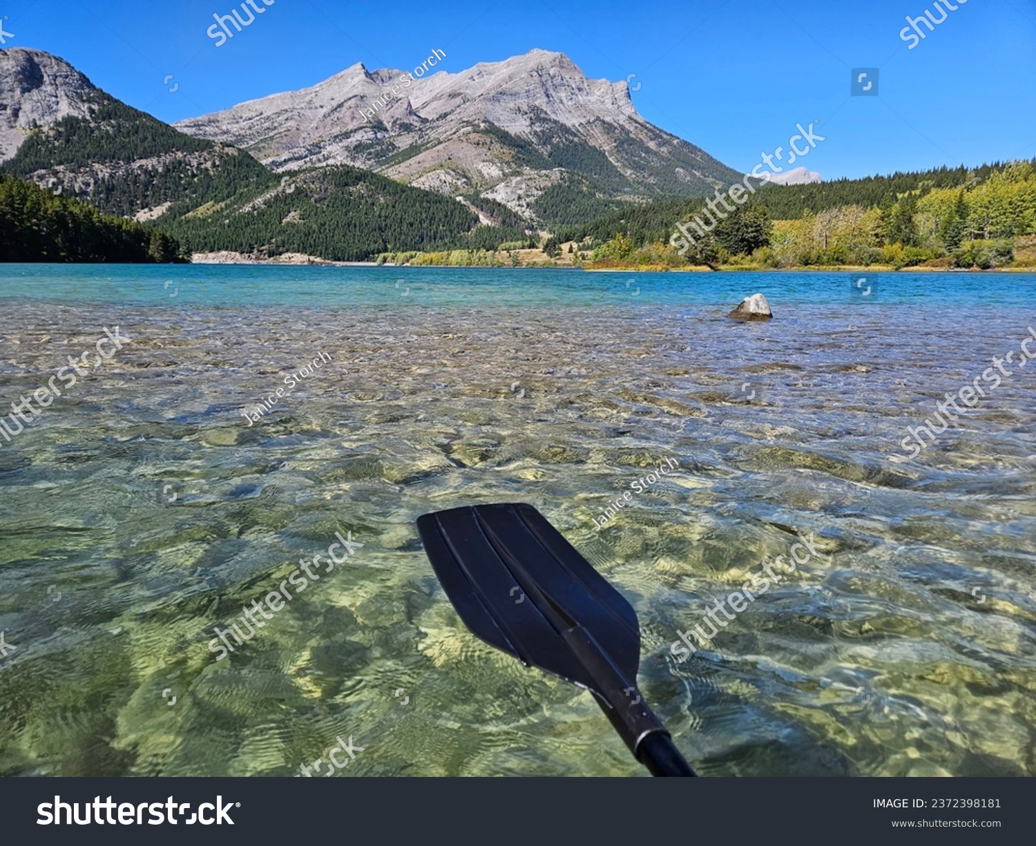 Outdoor watersport recreational image of a black plastic kayak paddle, a clear freshwater lake and a mountain range in the background. #2372398181