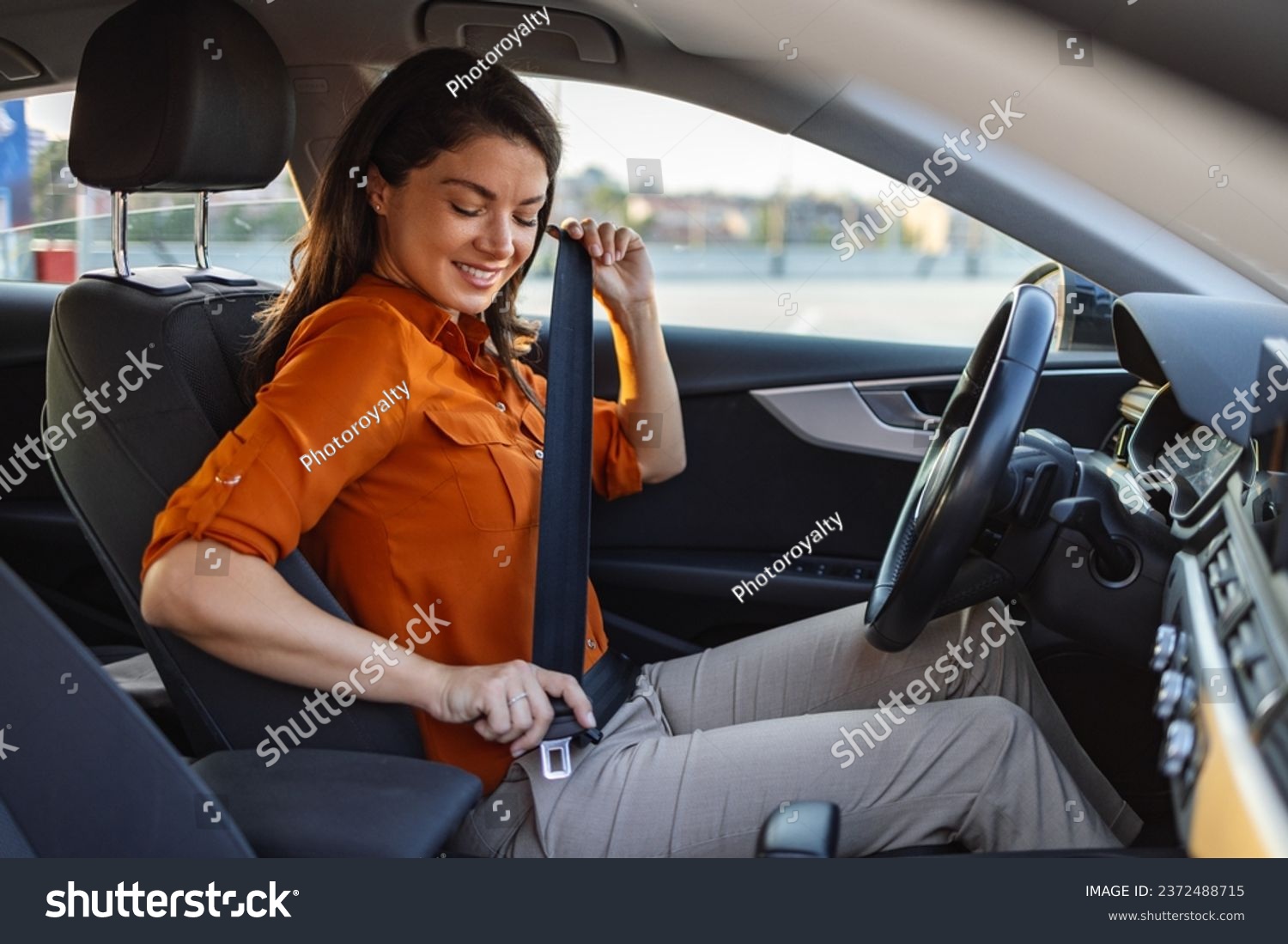 Young woman sitting on car seat and fastening seat belt, car safety concept. Woman fastens a seat belt in the car. Caucasian woman driver fastening car seat belt while sitting behind the wheel. #2372488715
