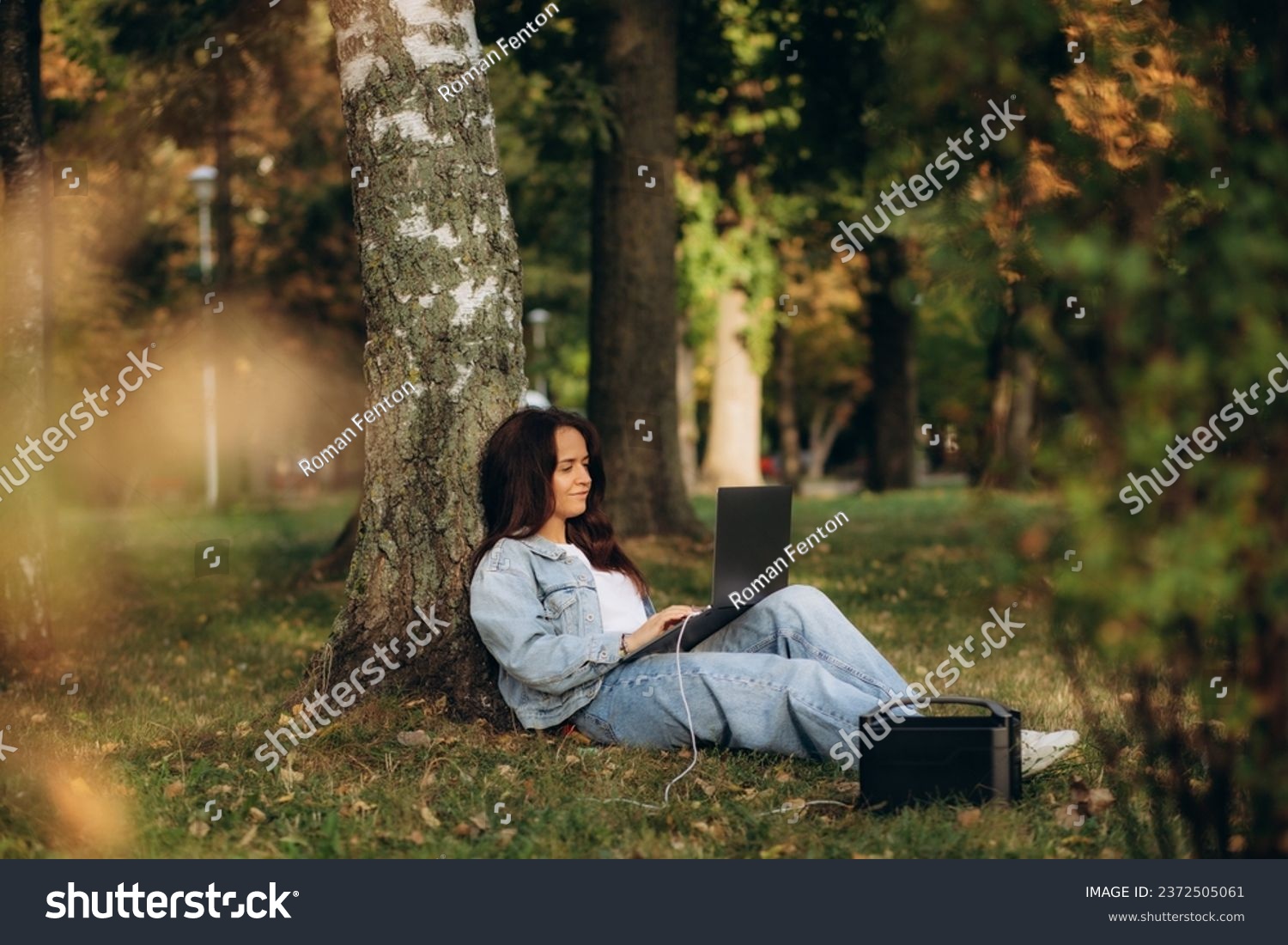 A woman in nature works on a laptop charging from a portable charging station #2372505061