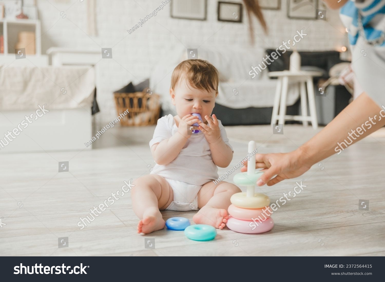 Beautiful young mother plays and teaches her baby 6 months old on the floor in the living room.mom and baby play with toys #2372564415